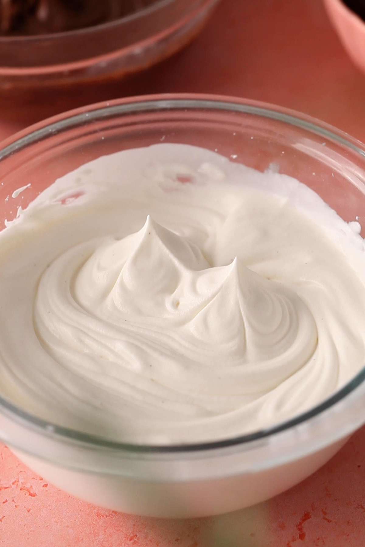 Whipped cream with stiff peaks in a glass bowl.