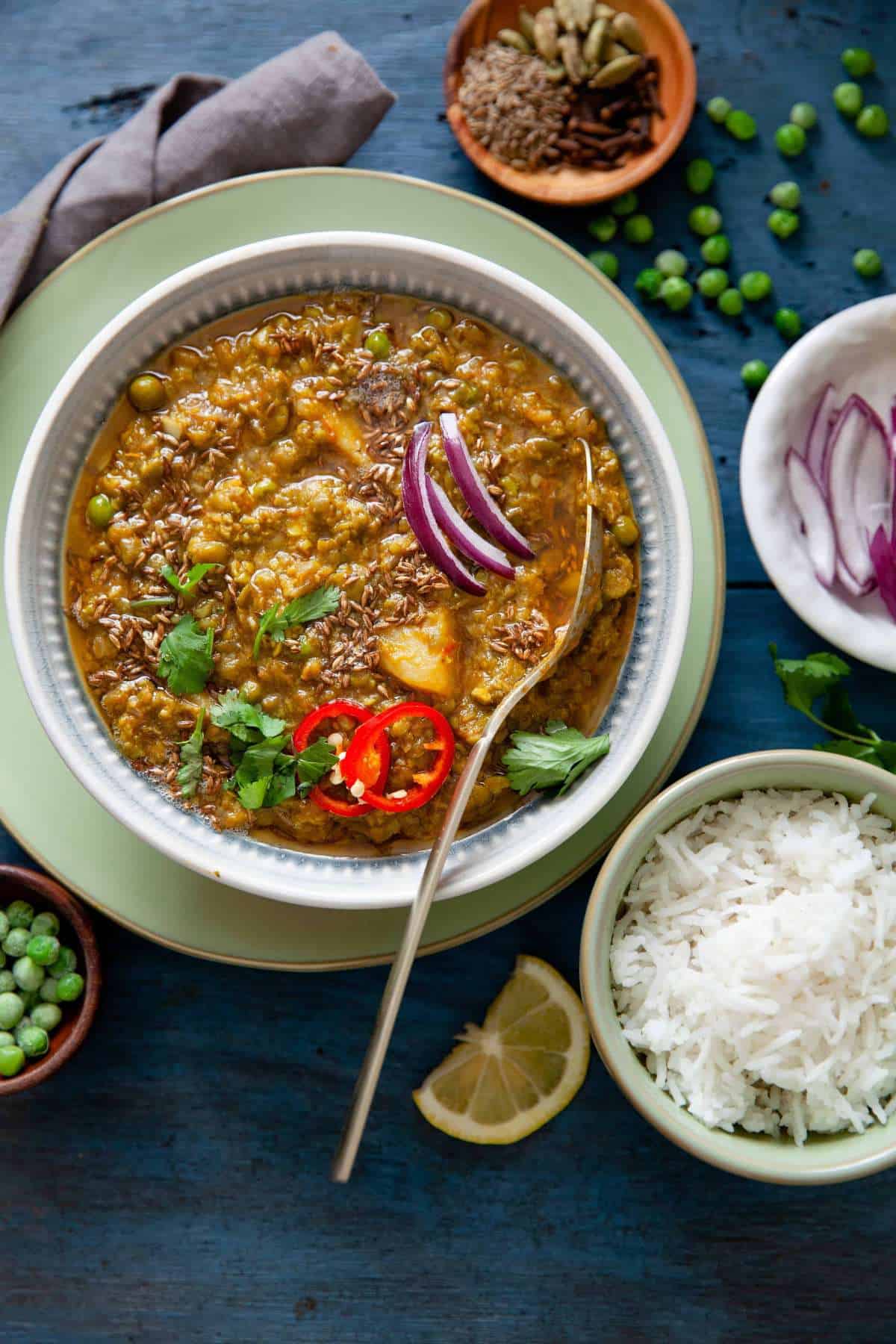 Matar Nimona served in a white bowl with sliced onion, red chillies and rice on side. 