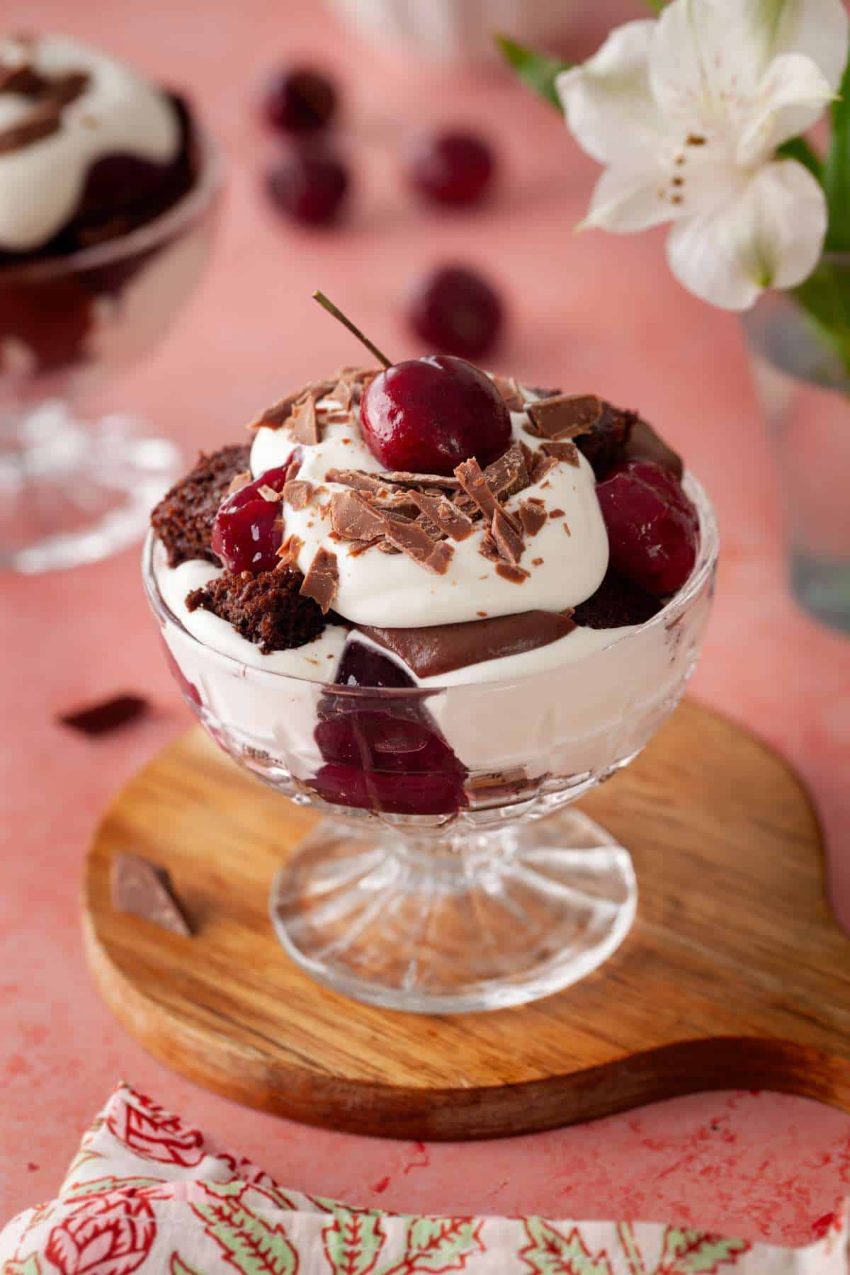 Black forest trifle in a glass bowl on a small brown board.