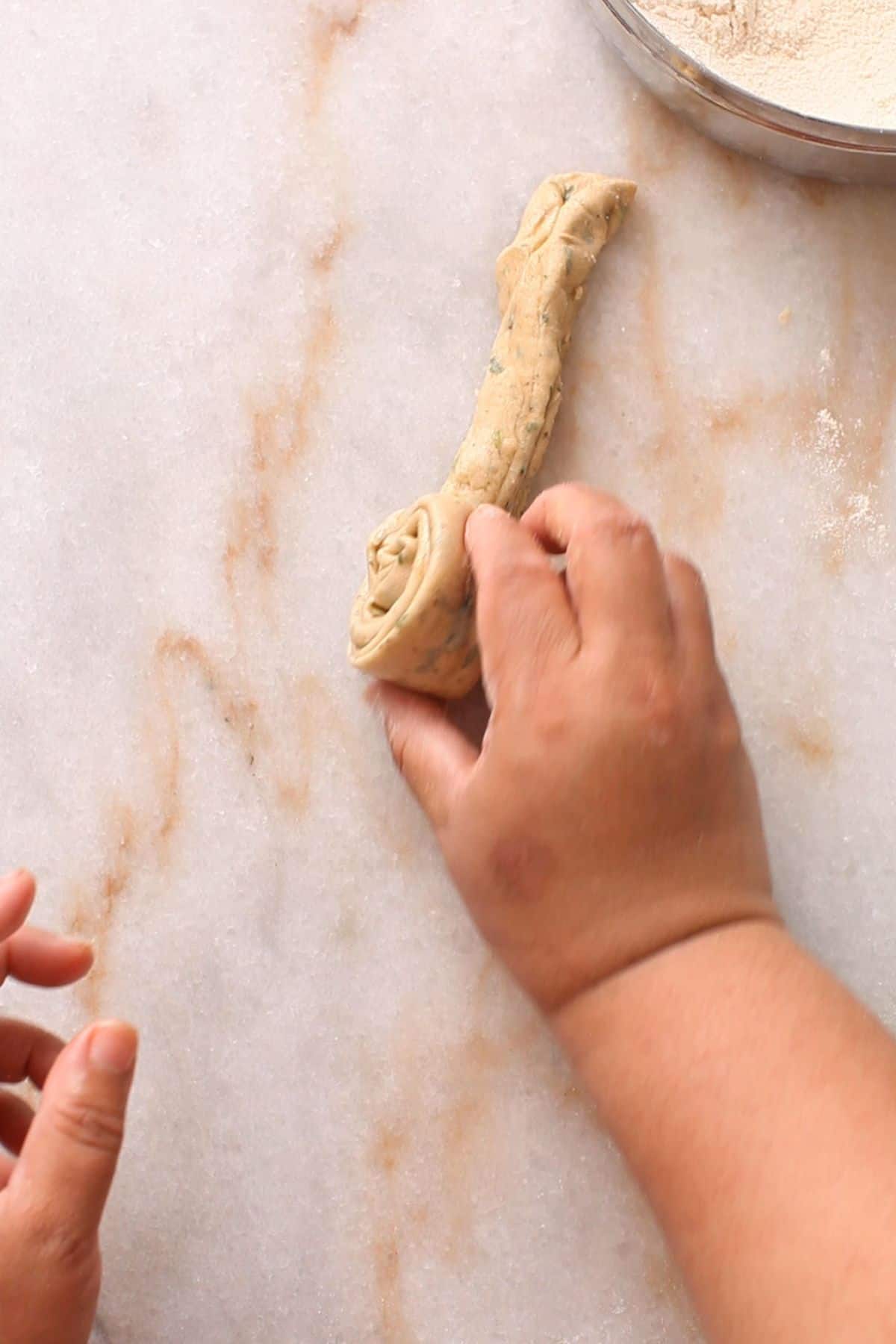 Rolling pleated dough  on a marble surface, shaping it into a spiral. 