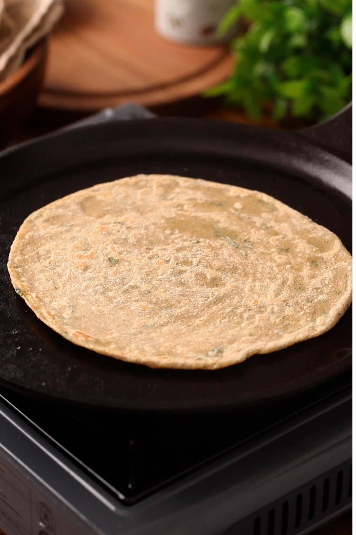 Uncooked mint flatbread is heating on a black skillet placed on a stovetop.