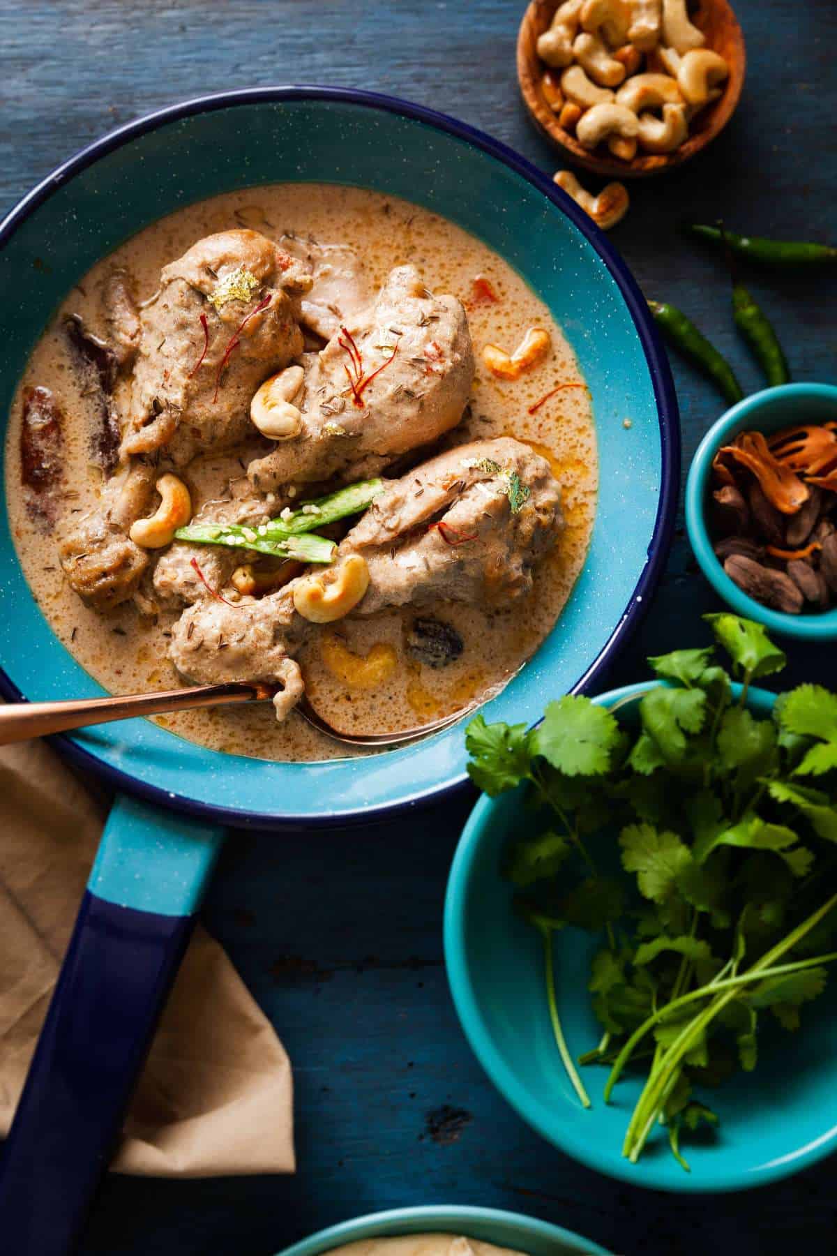 Chicken rezala served in a blue pan garnished with saffron and green chillies. 