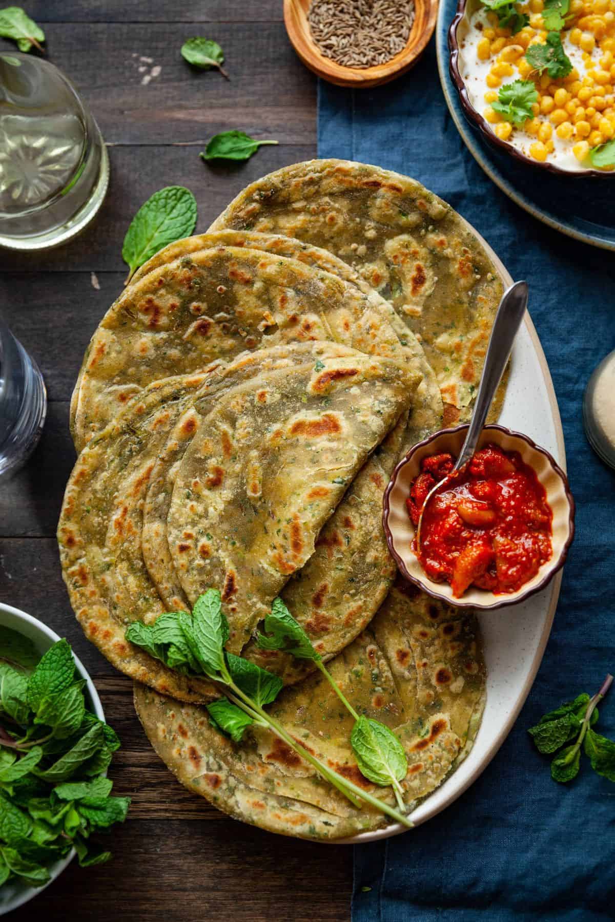 Laccha Pudina Paratha placed on a oval platter with garlic pickle and a sprig of fresh mint.
