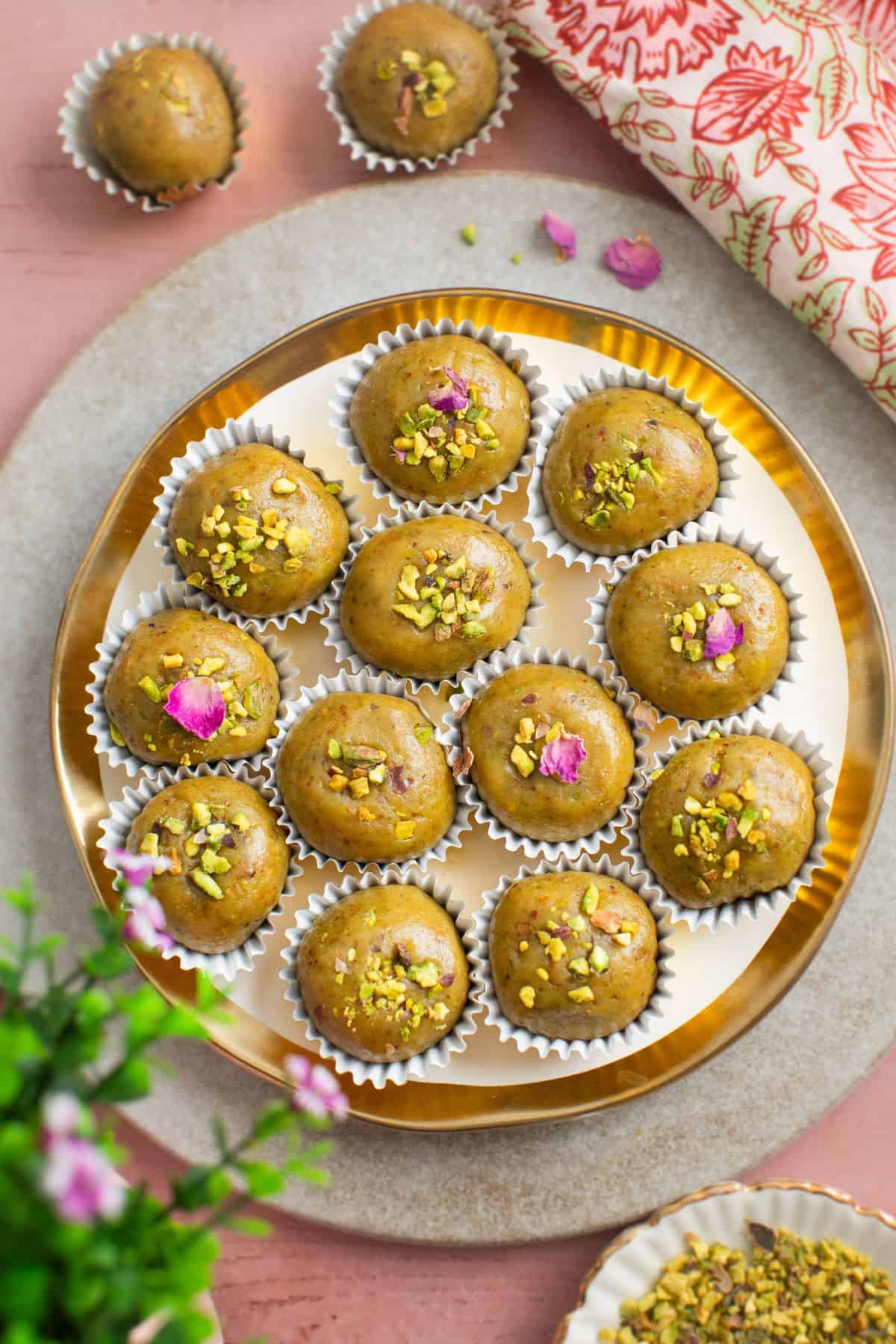 Pistachio Ladoo placeed on a gold and white plate over a pink background.