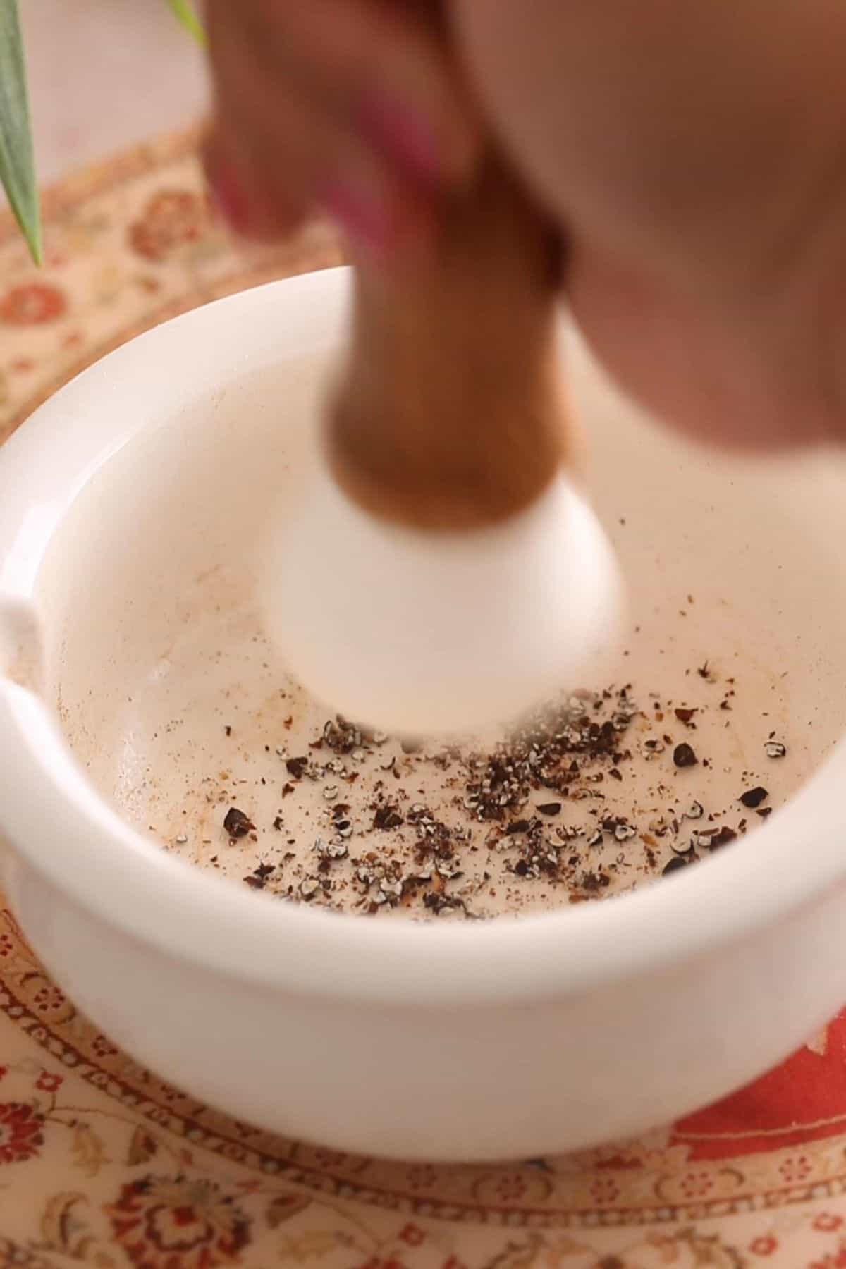 Grinding black cardamom seeds using mortar pestle.