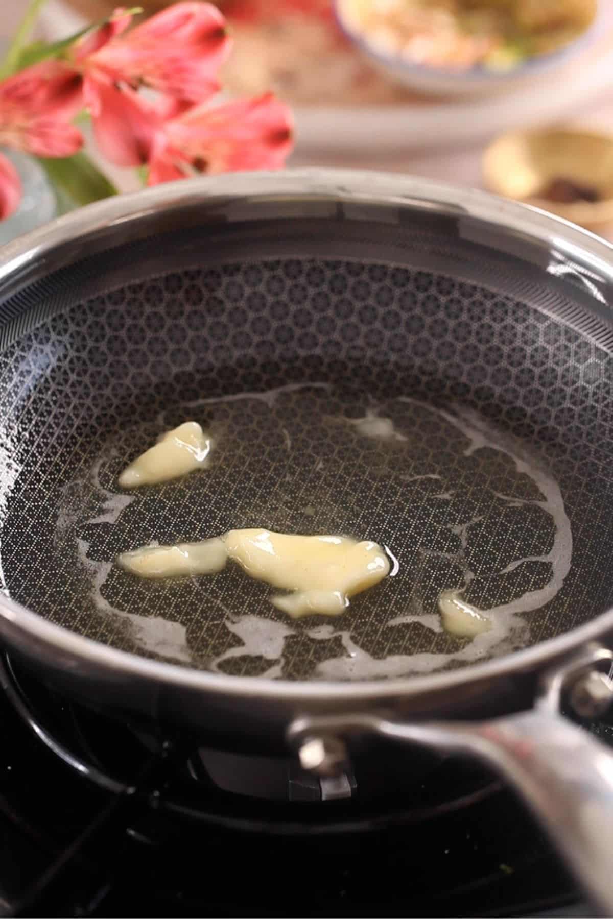 Ghee is melting in a black steel pan.