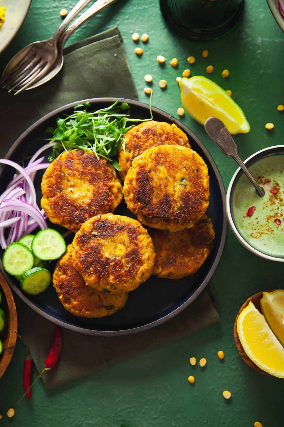 Lentil patties served on a black plate with onion cucumber and lemon.