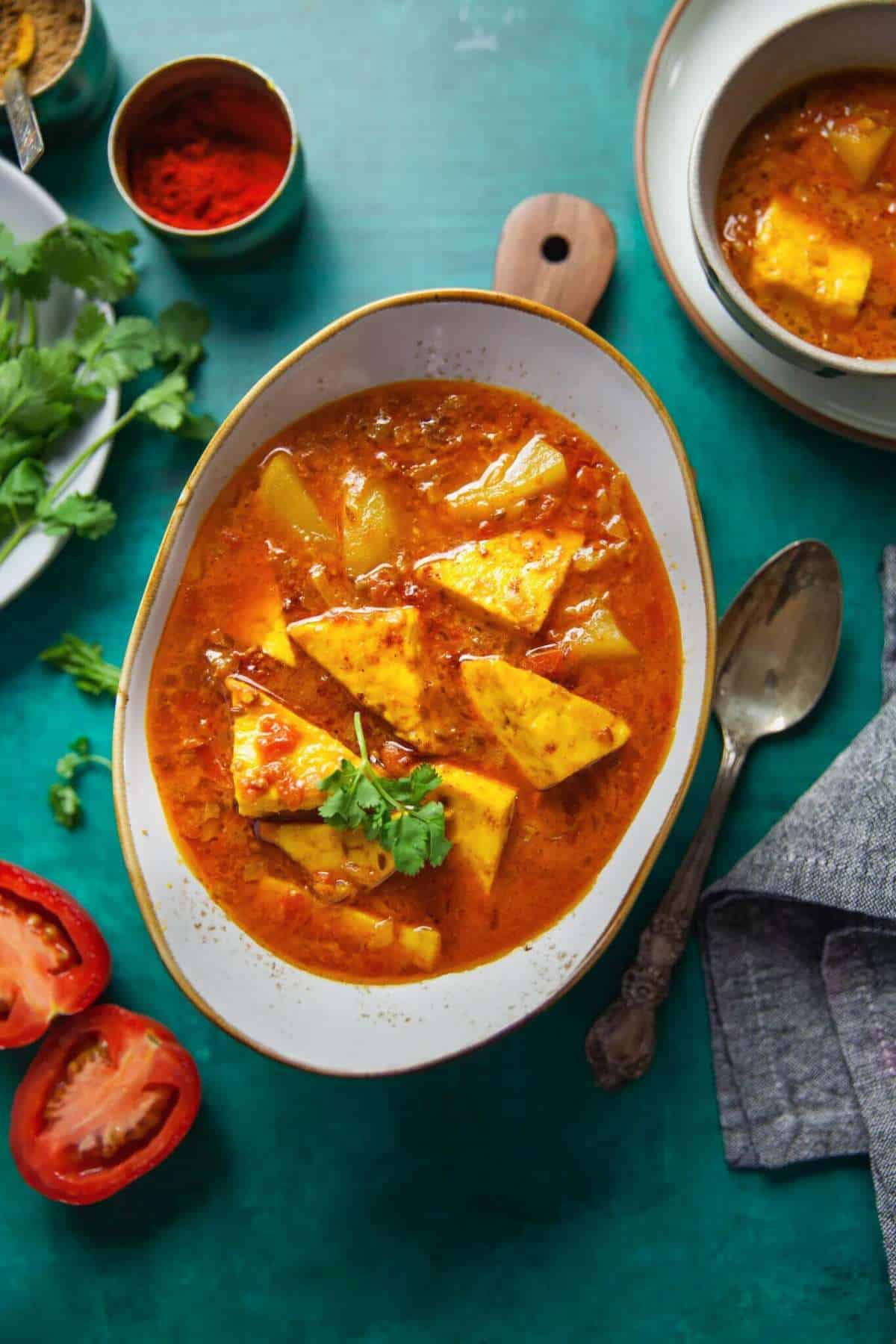 Aloo Paneer Curry served in an oval white dish on green background.
