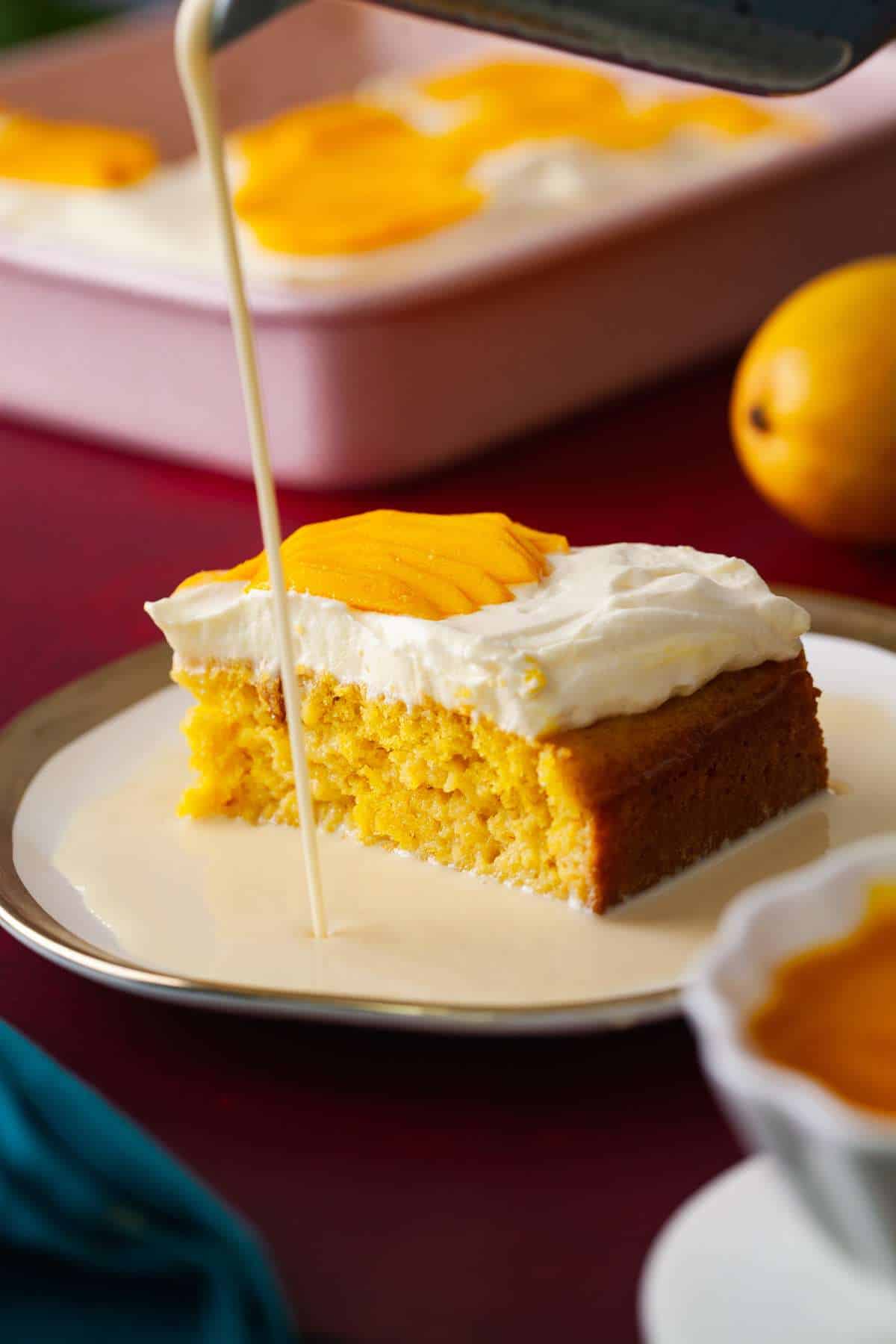 An image of mango fresh leches cake slice being drizzled with 3 milk mixture. 