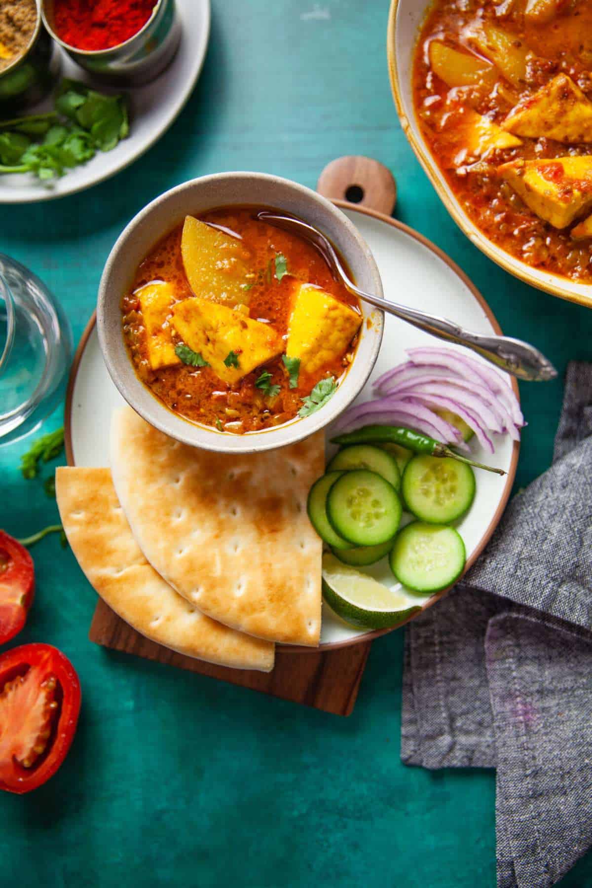A bowl of paneer aloo curry with salad and flatbreads.