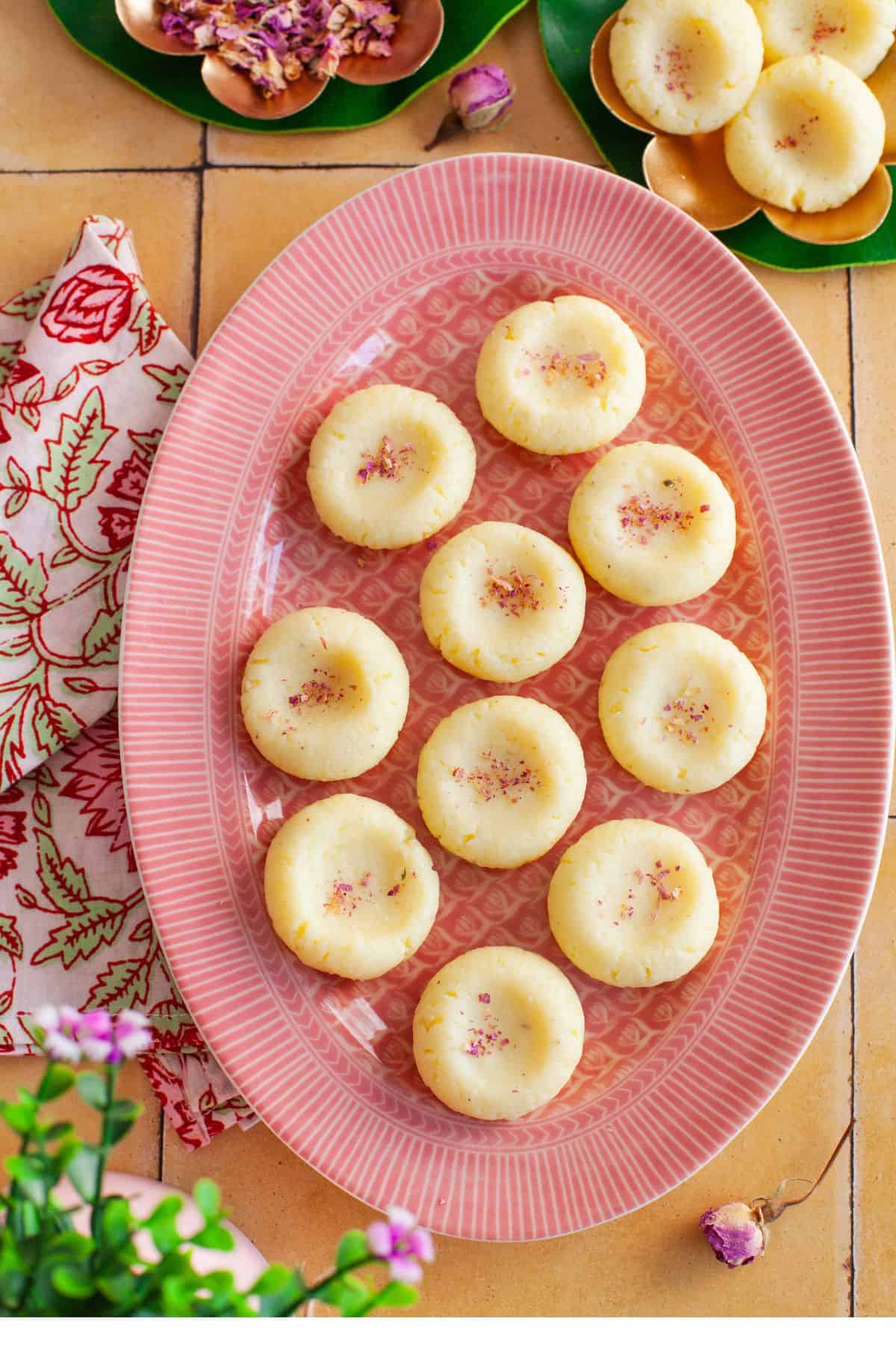 Creamy cardamom peda served on a pink plate placed on a yellow tiled background. 