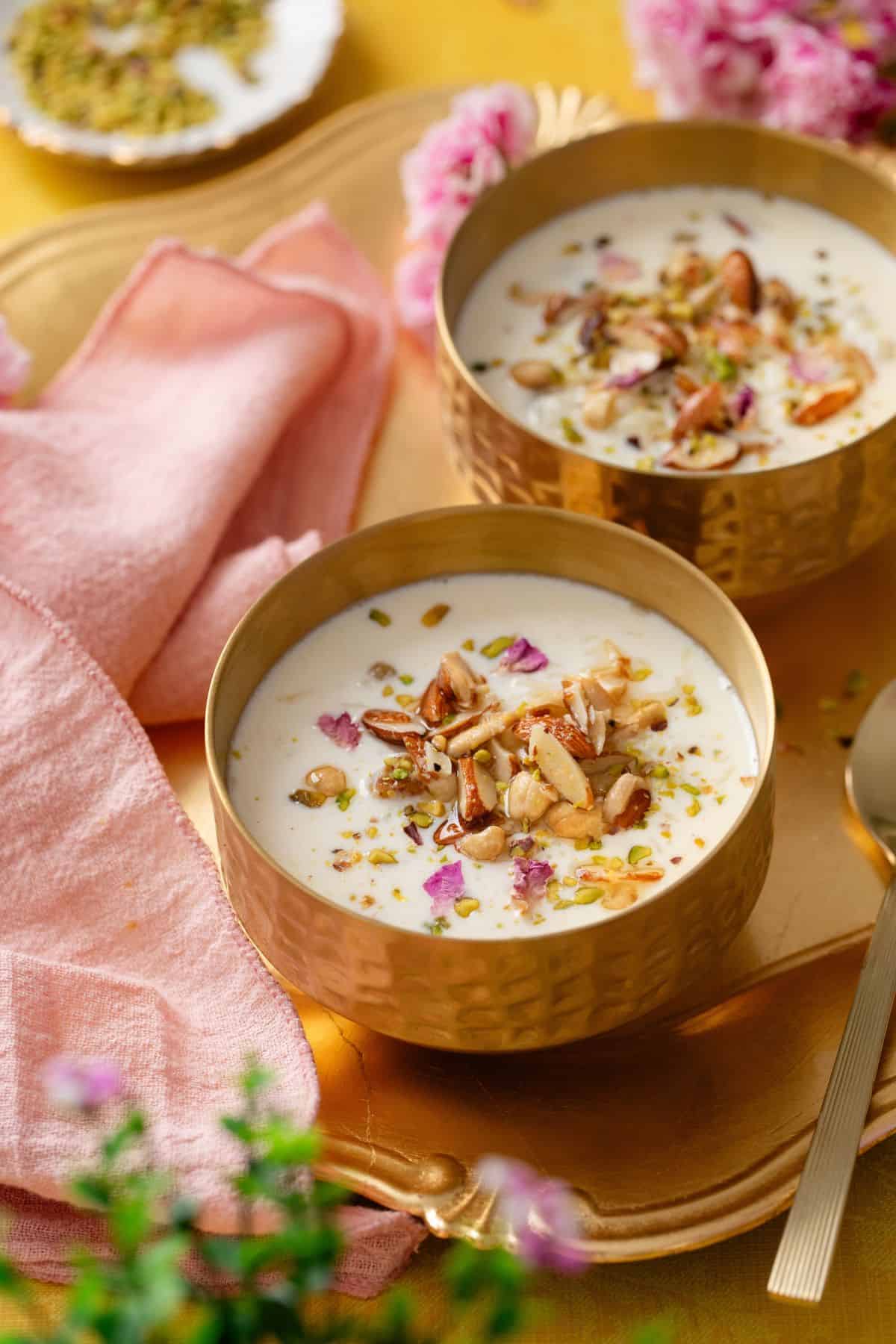 Rice Kheer served in two gold bowls and garnished with chopped nuts and raisins.