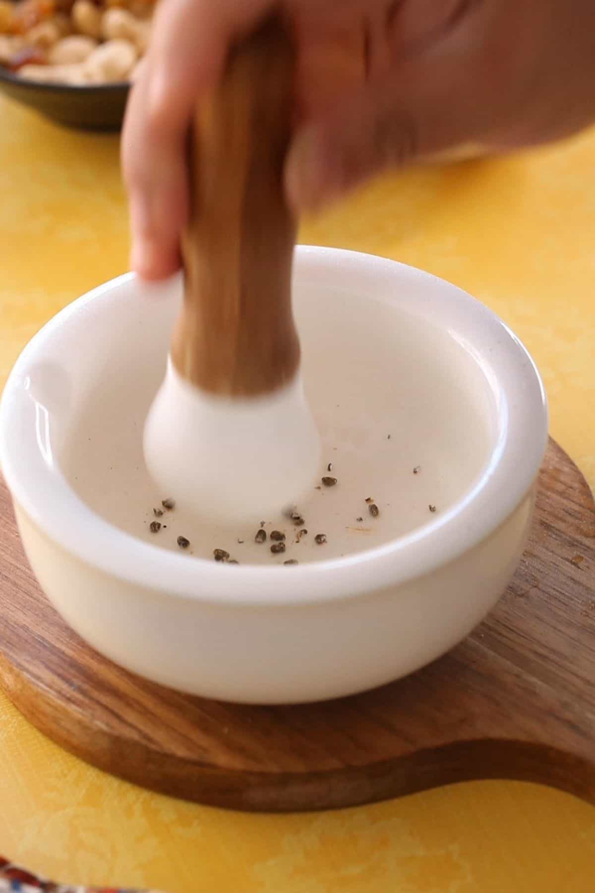 Green cardamom seeds in a white mortar pestle. 