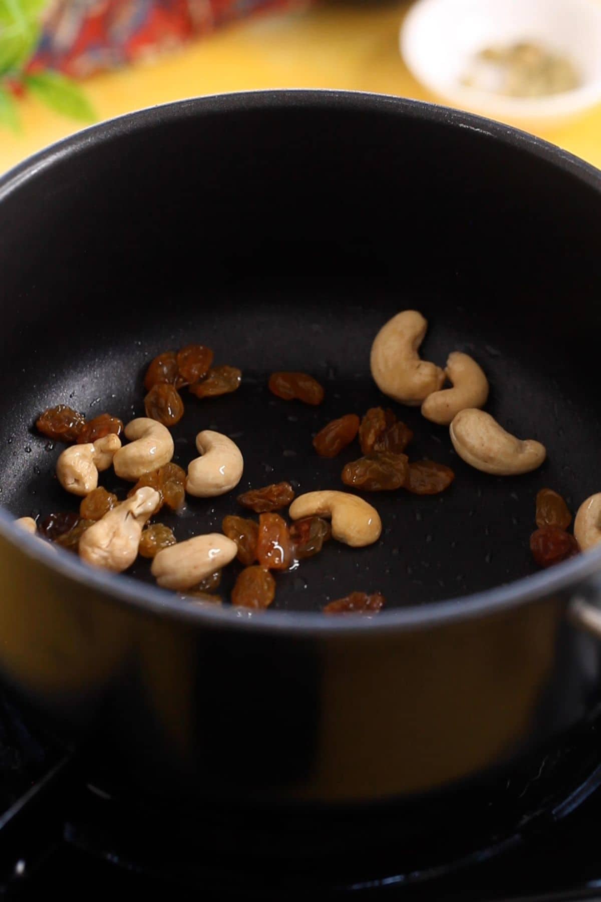 Cashews and raisins sauteing in ghee in a black sauce pot.