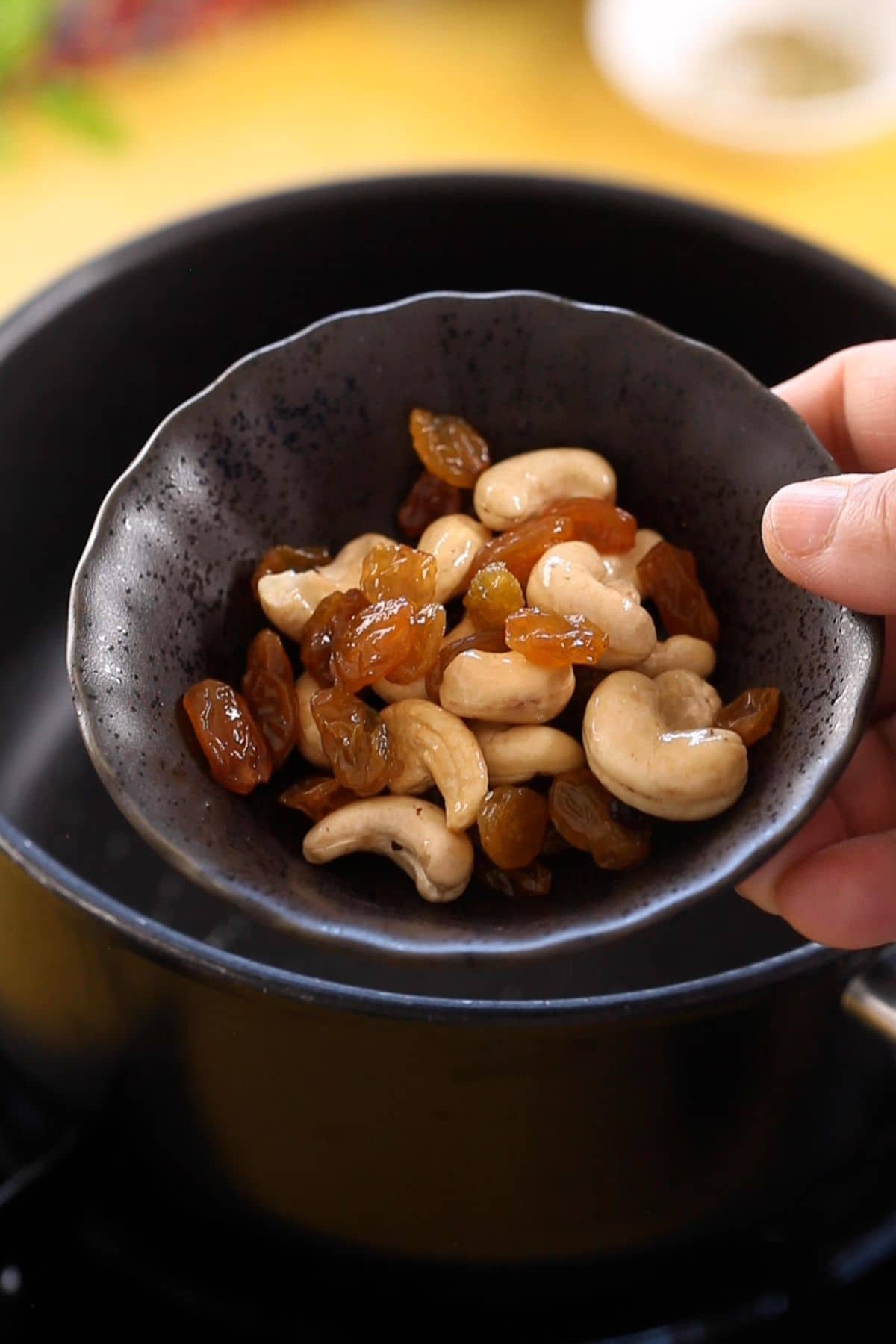 Browned cashew and raisins in a black pinch bowl.