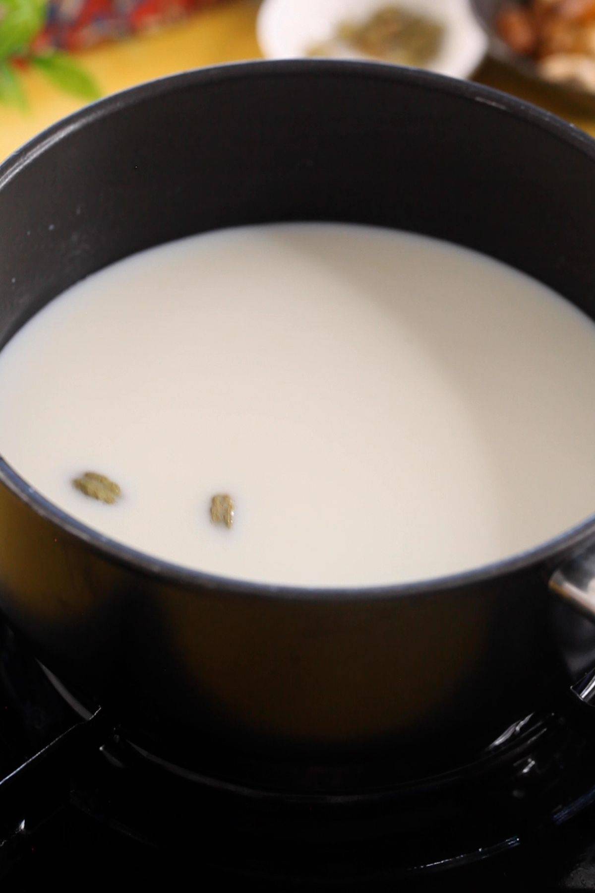 Whole milk and green cardamom pods in a black sauce pot.