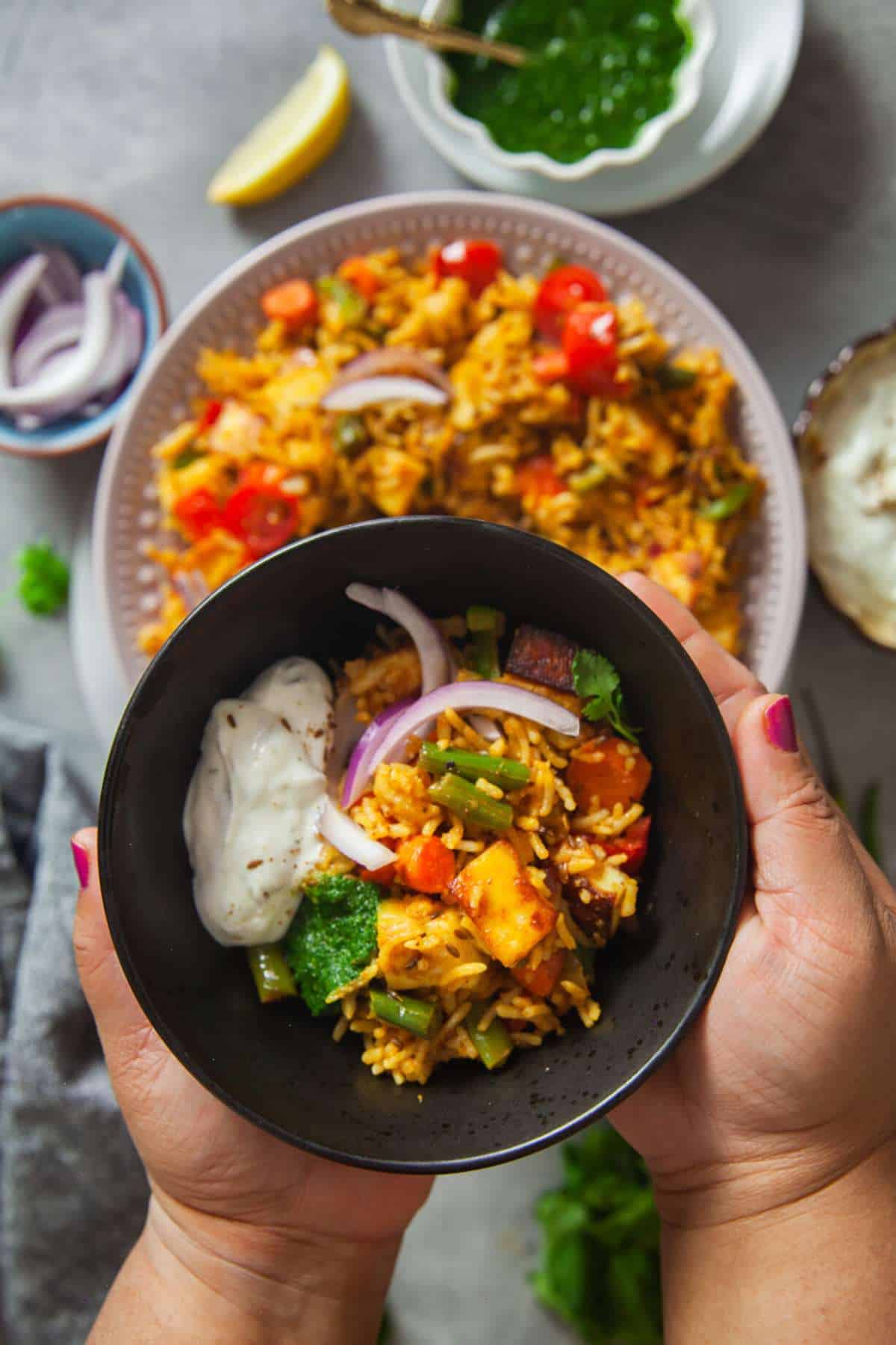 Holding a black bowl of paneer tawa pulao.