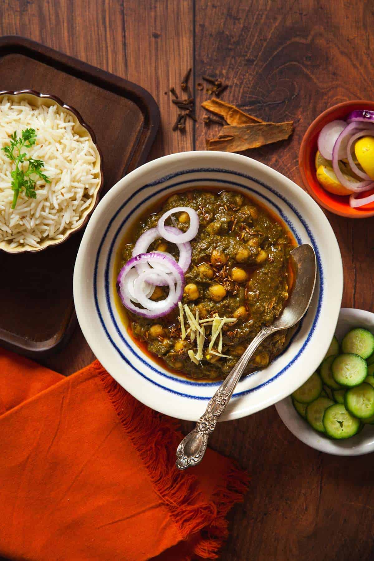 Palak Chole served in a white bowl with rice, cucumbers and steamed rice. 