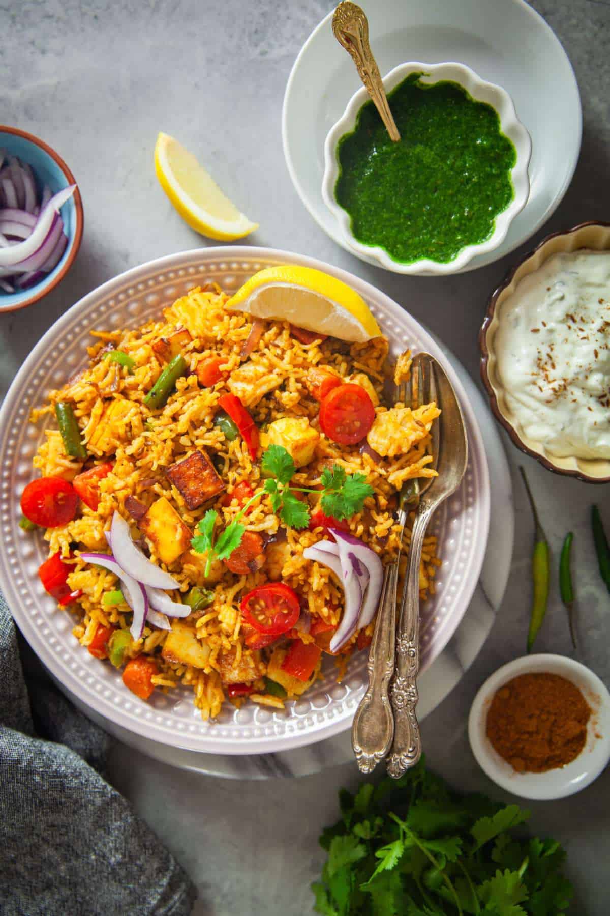 Tawa pulao served in a plate with green chutney and yogurt.