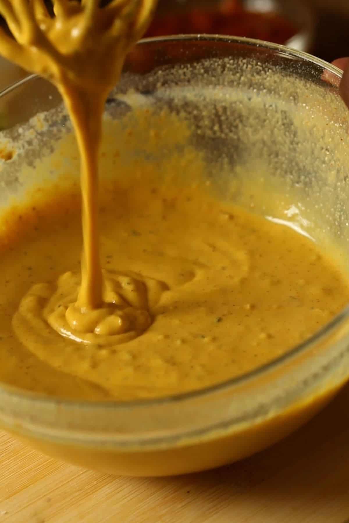 Pakora batter is dripping from a metal whisk and flowing like a ribbon.