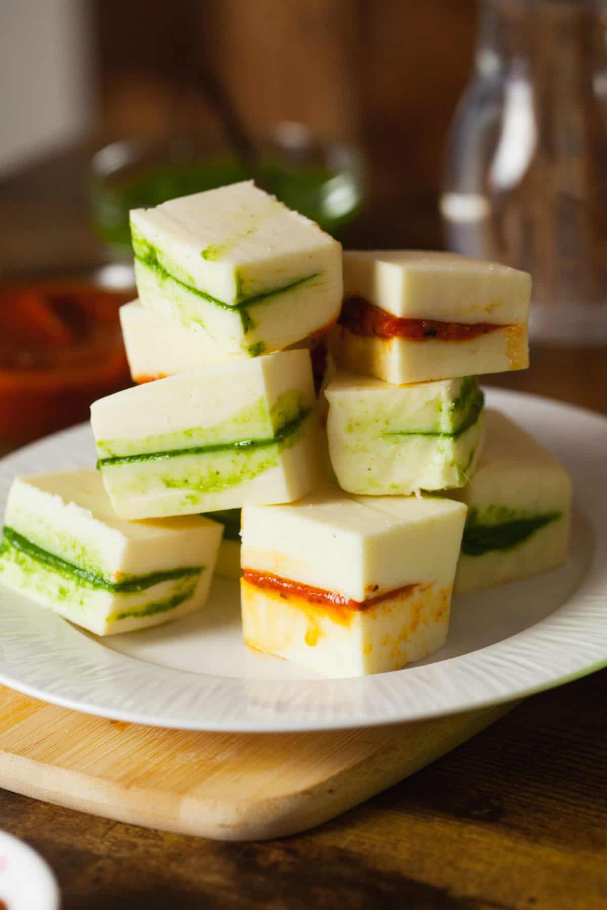 Green chutney and tomato chutney stuffed paneer pieces placed in a stack on a white plate.