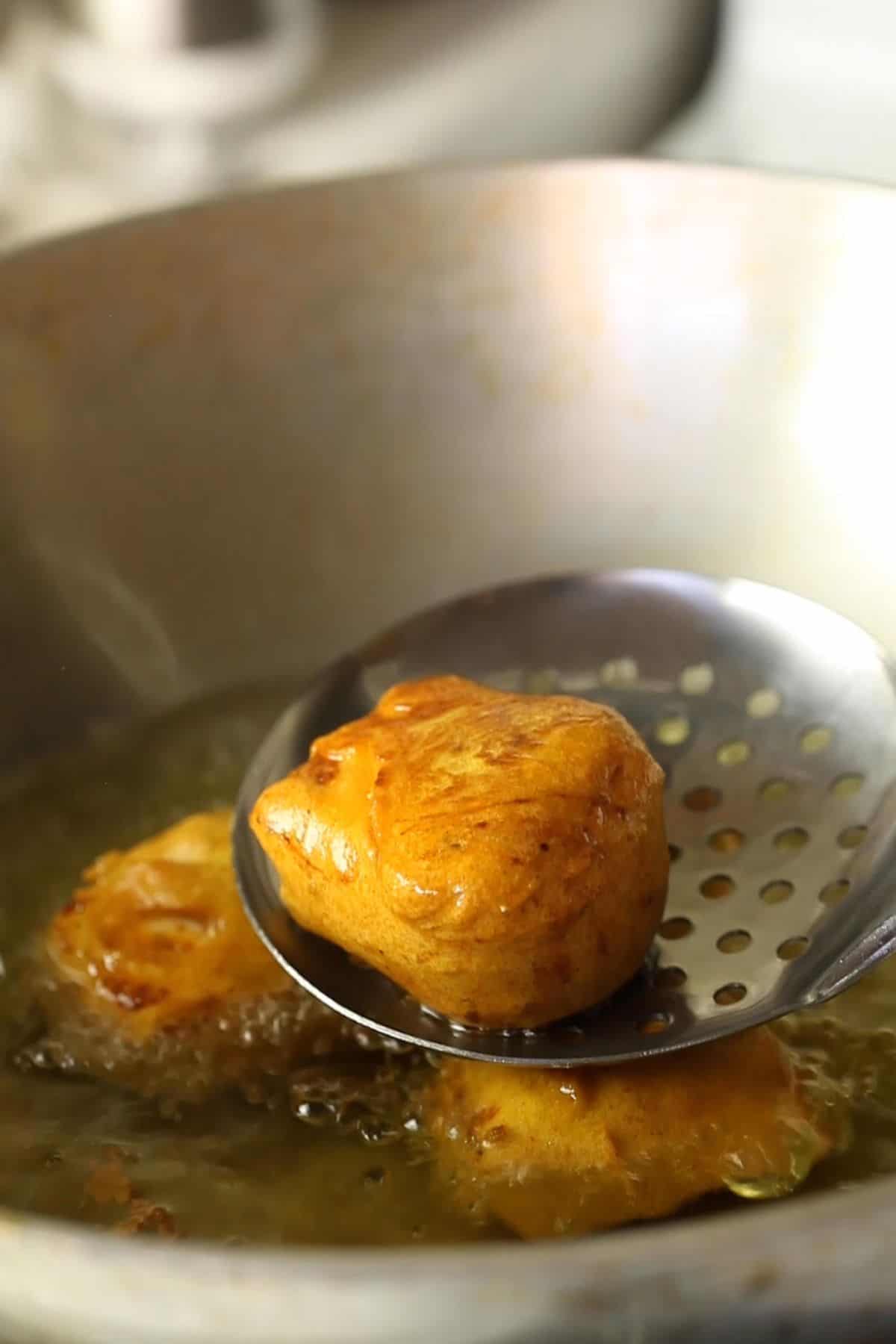 Paneer pakora are being deep fried in hot oil in a kadai.