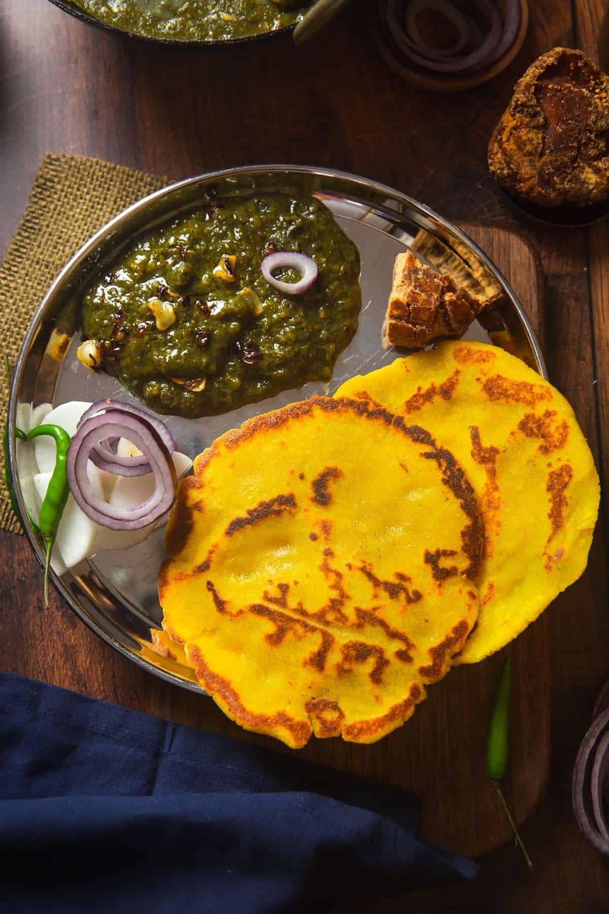 Sarson Ka saag served in a steel plate with salad, jaggery and makki roti.