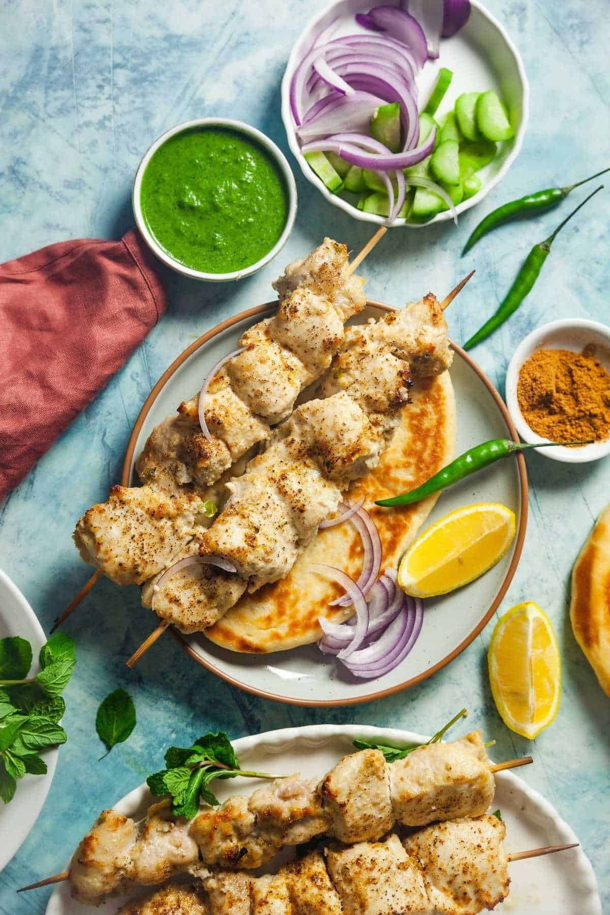 Chicken Malai Tikka plated on a white plate with naan & green chutney.