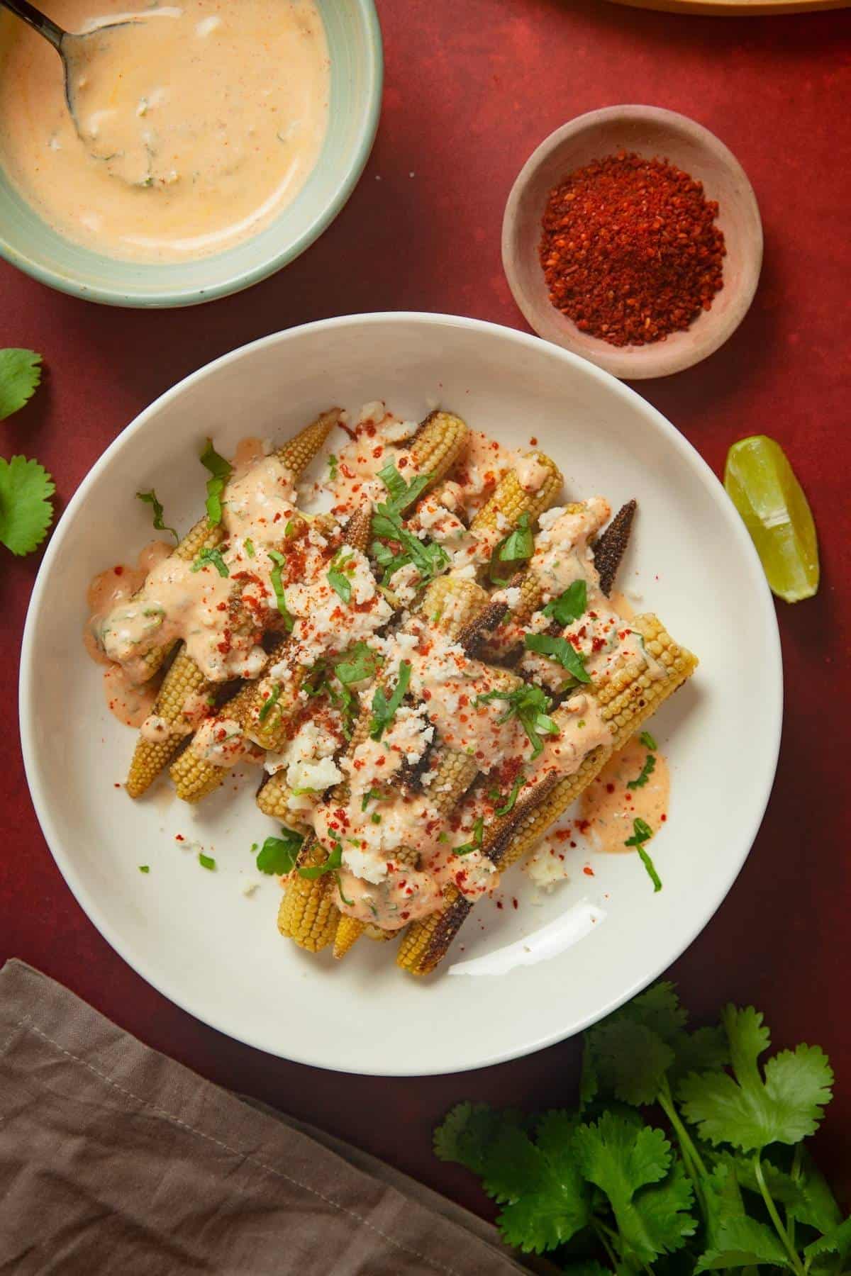 Baby Corn Elote with cheese sauce, lime wedges and cilantro