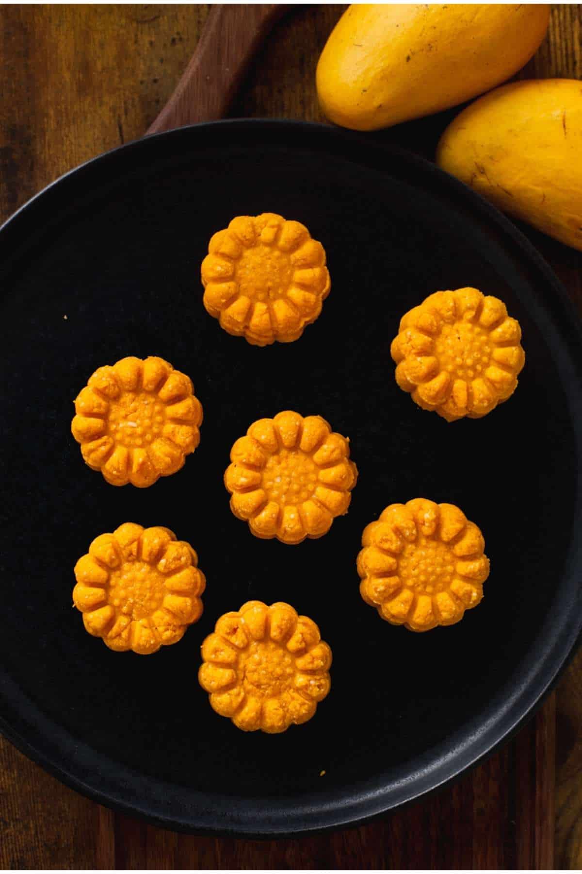Flower stamped mango sandesh on a black platter.