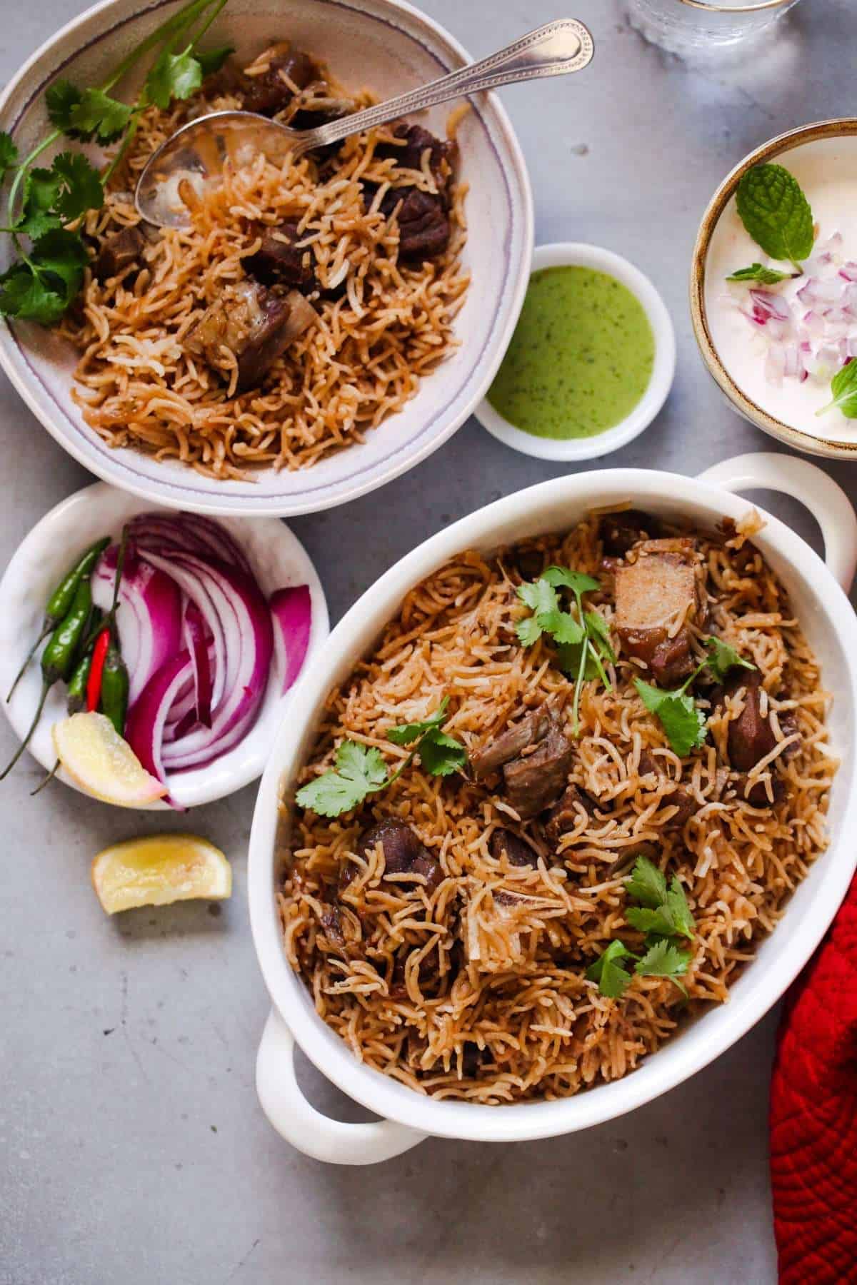Yakhni Pulao in an oval dish with sliced onions and side of raita (yogurt).