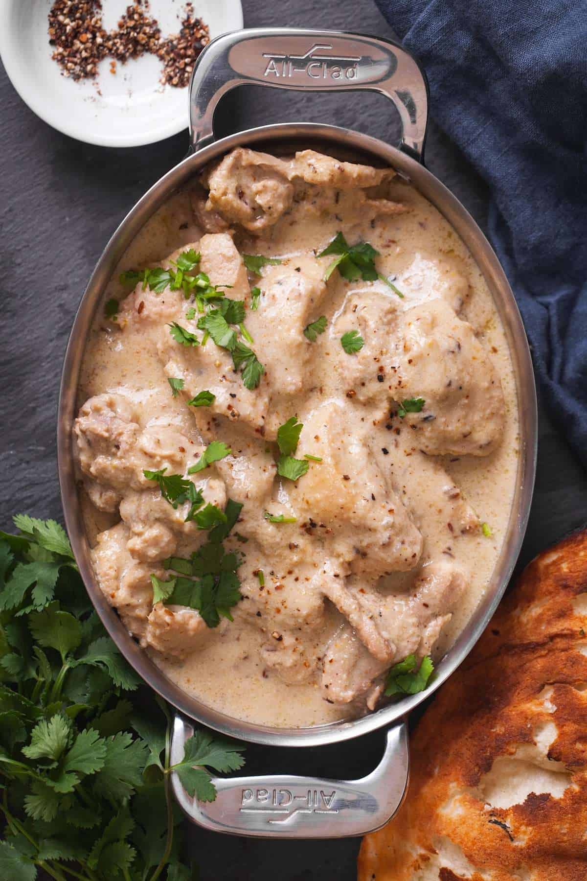 Chicken Kali Mirch in a oval steel dish With Naan and Cilantro.