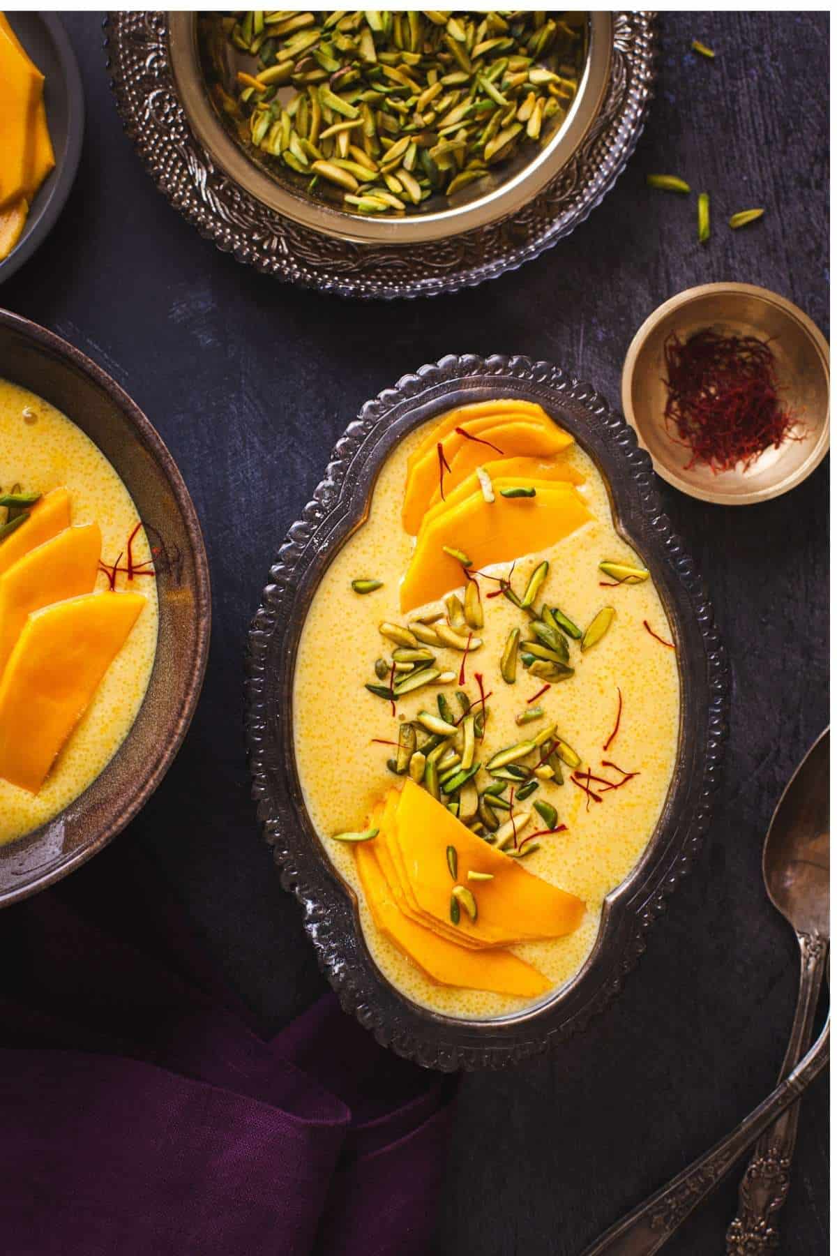 Mango Phirni in a oval silver bowl garnished with pistachios and saffron. 