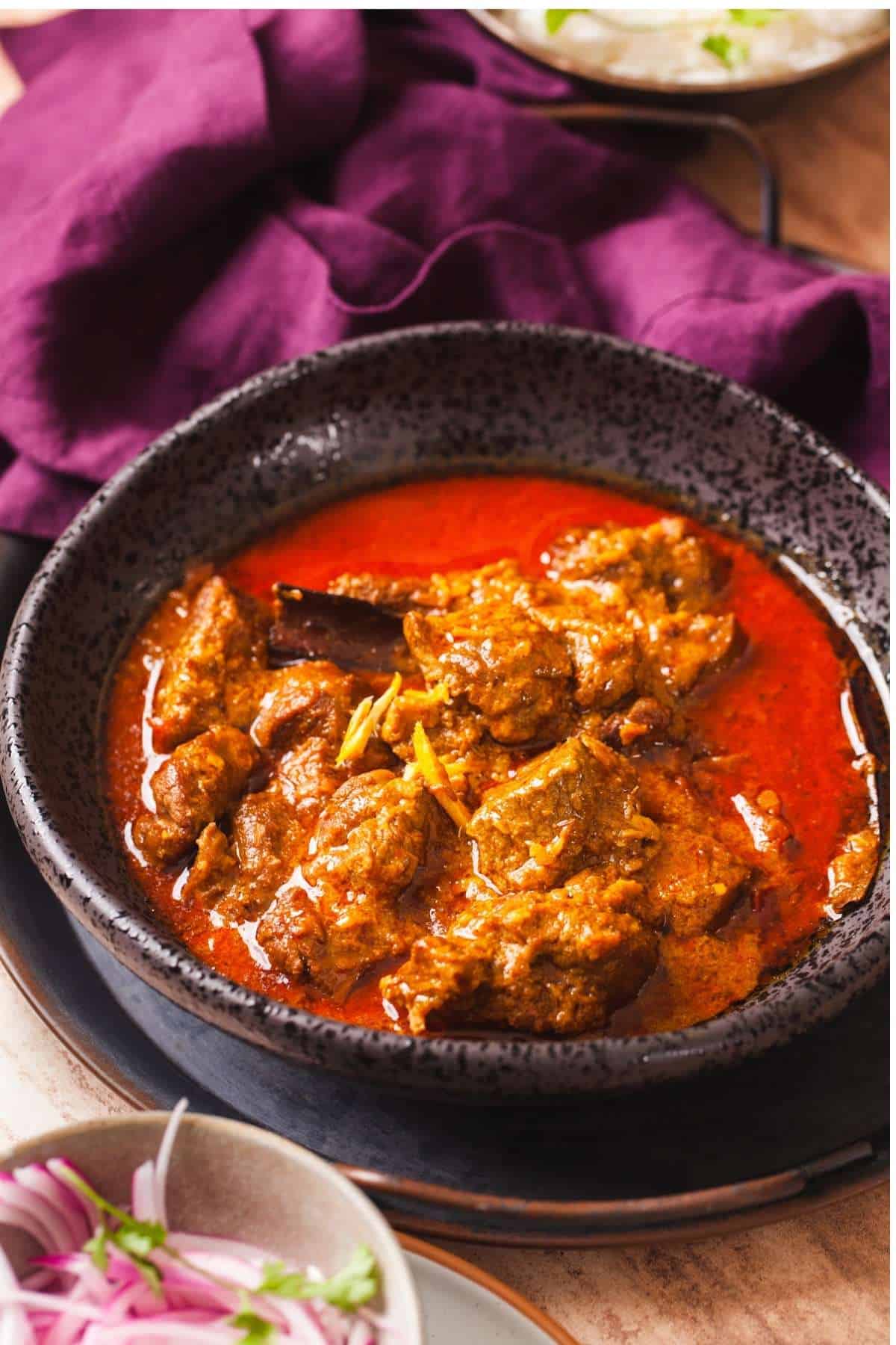 Side shot of Indian Lamb Curry in a black bowl with onions and rice. 