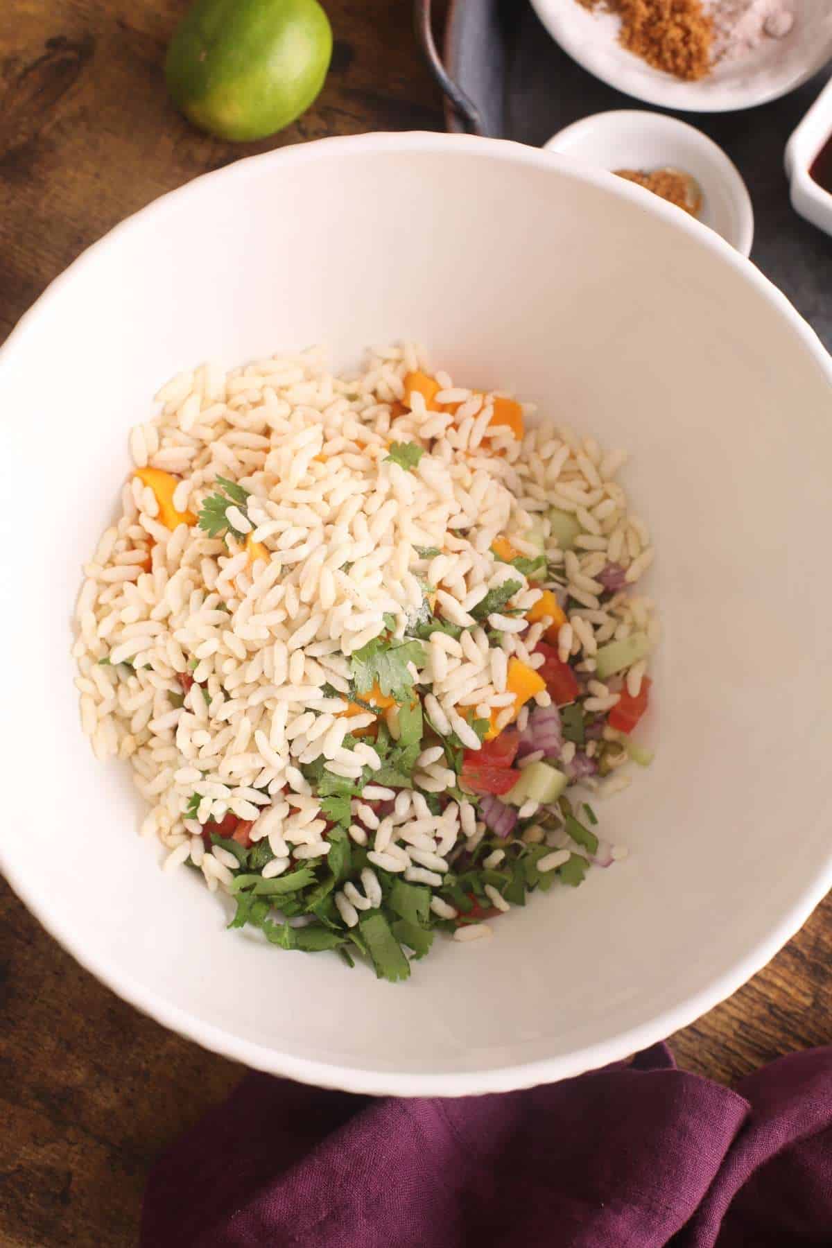 Mixing chaat ingredients like sprouts, rice puff and vegetables in a large bowl.