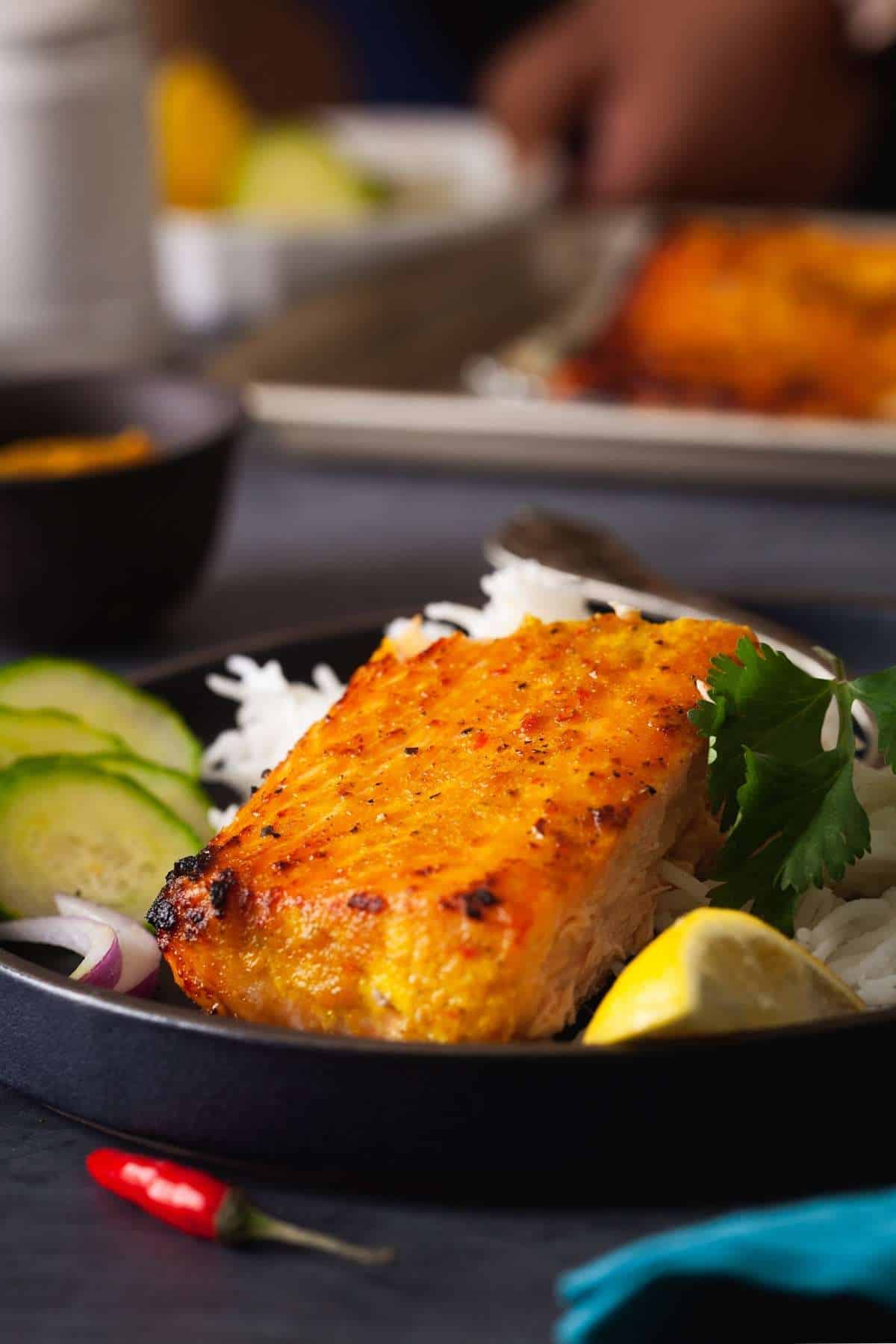 Side shot of Salmon plated on a black plate with rice, leon and cucumber.