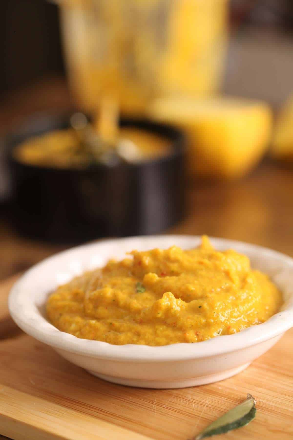 Side shot of fresh ground masala made with ginger, garlic, chilies, curry leaves and coconut oil in a small white dish.