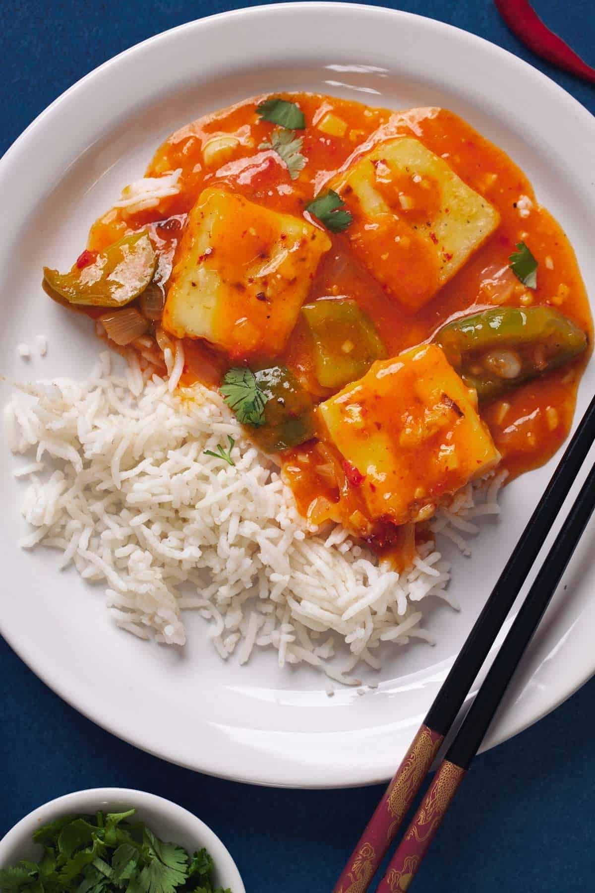 Paneer in Hot Garlic Sauce serve with jasmine rice on a white plate with chopsticks.