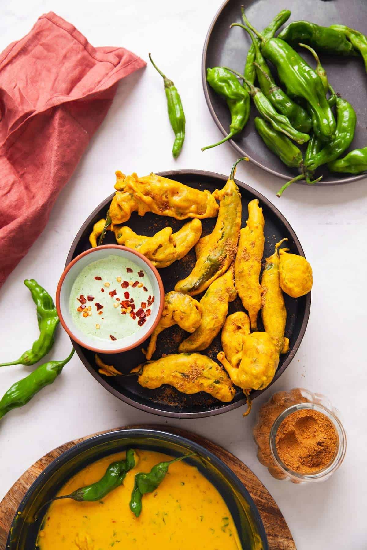Shishito Pepper Pakora Recipe with creamy yogurt dip placed on a black plate on a white background. 