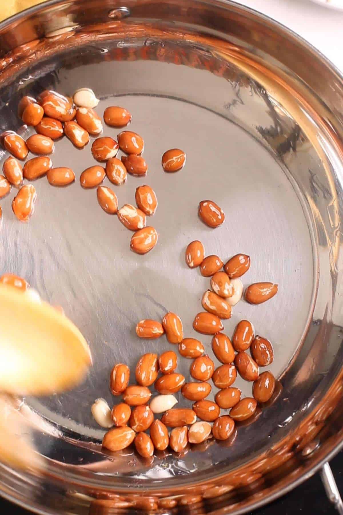 Roasting peanuts in ghee in a stainless steel kadai.