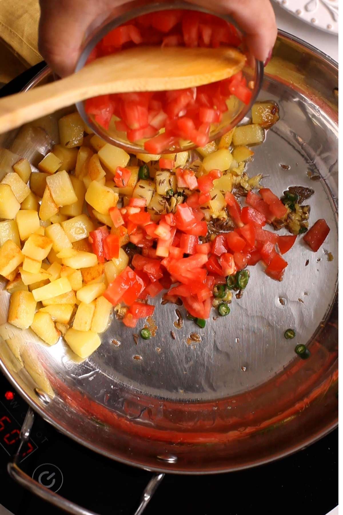 Diced tomatoes are added to spices and potatoes.