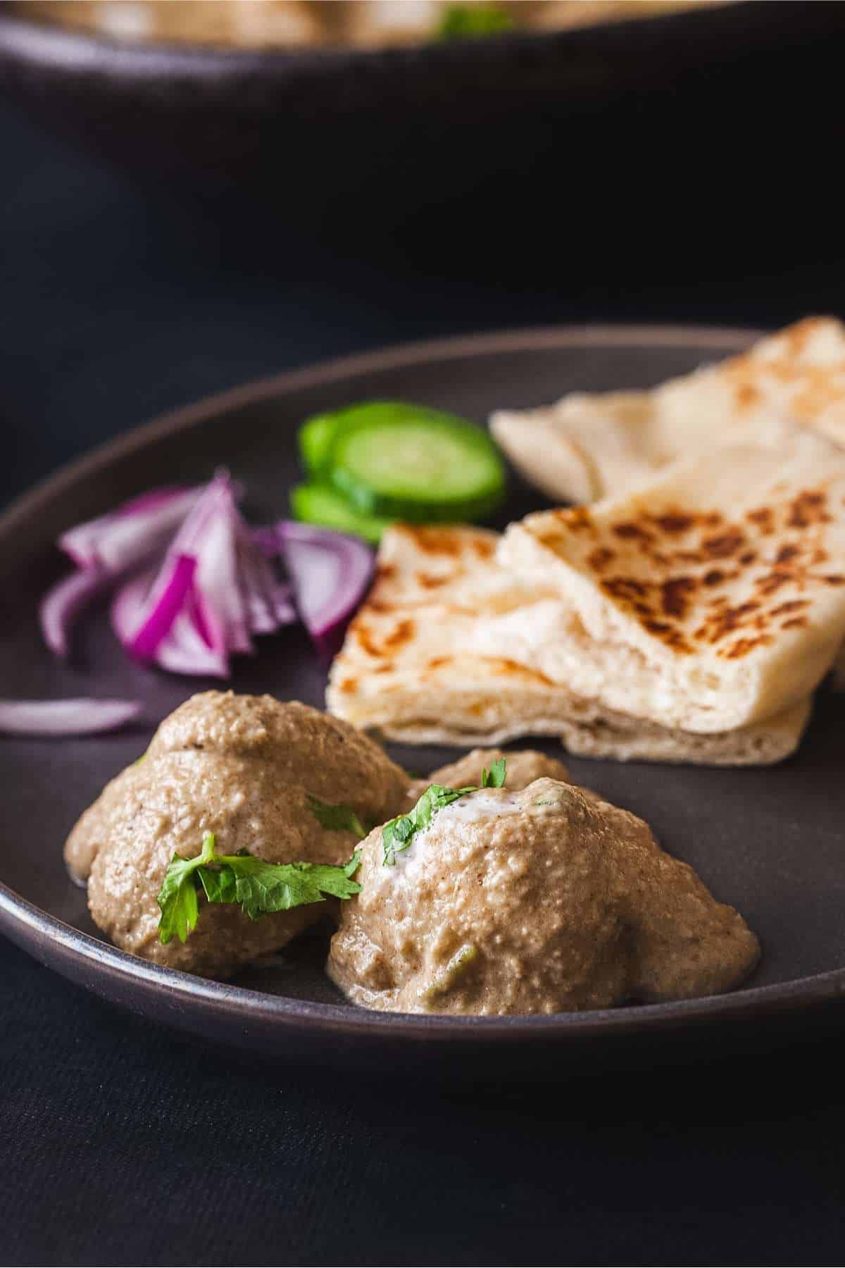 Malai Aloo served with naan on a black plate.