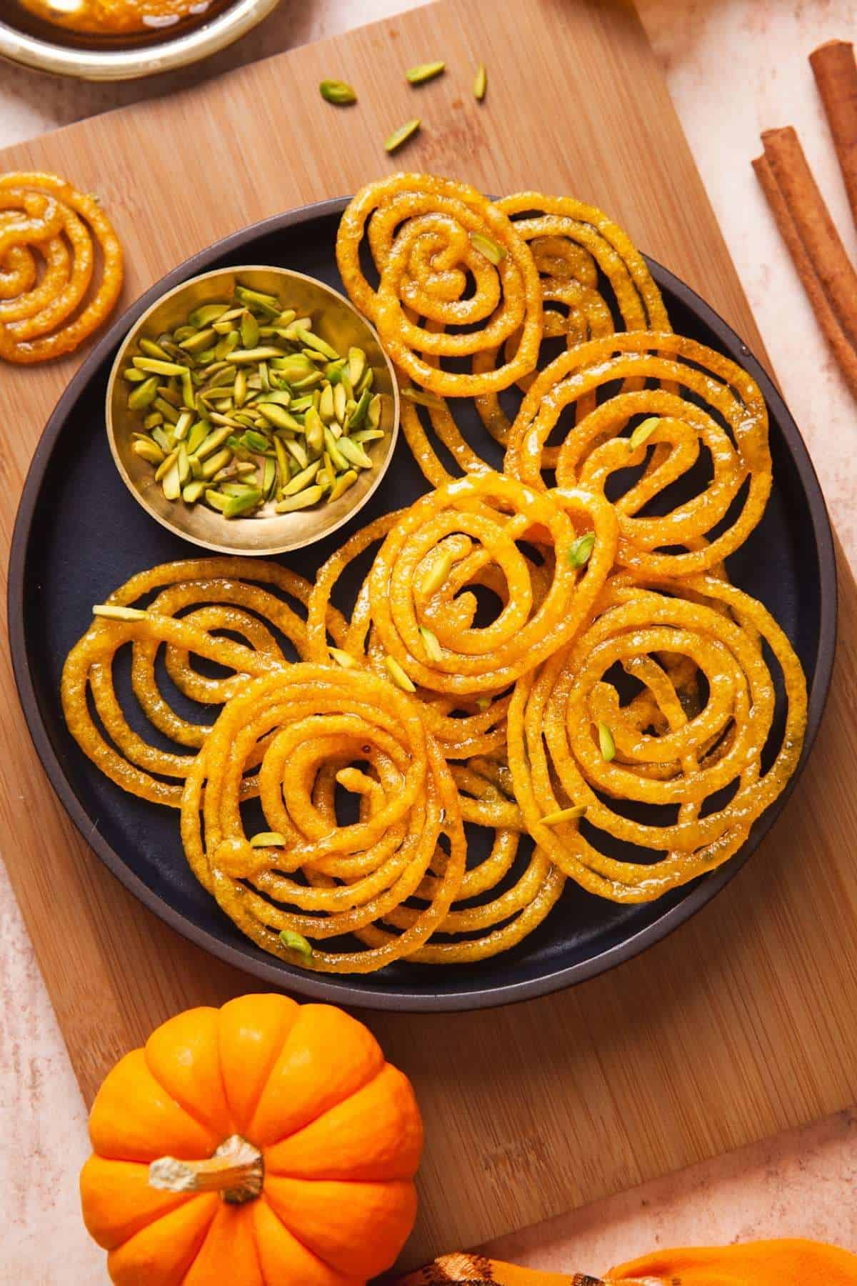 Indian Fusion Pumpkin Jalebi on a black plate with a bowl of silvered pistachios.