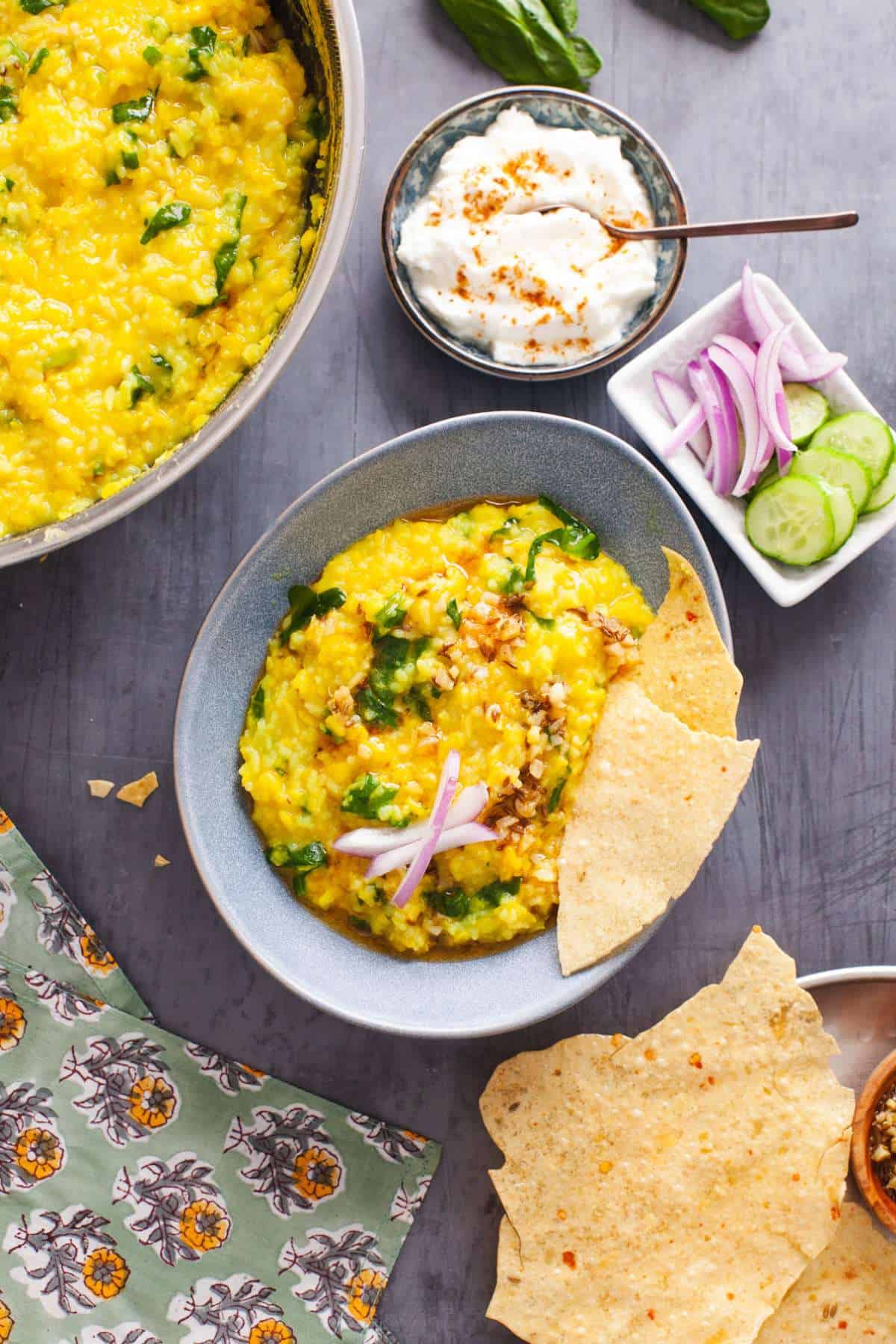 Yellow Moong Dal Khichdi With palak served with papadam and onions in a egg shaped blue bowl.