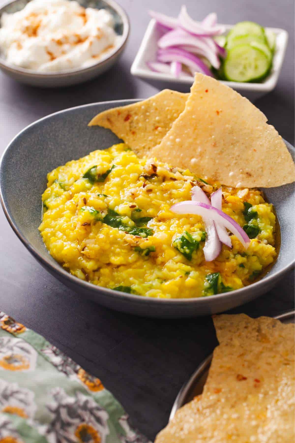 Side Shot of mung dal khichdi with onions slices, tadka and papadams.