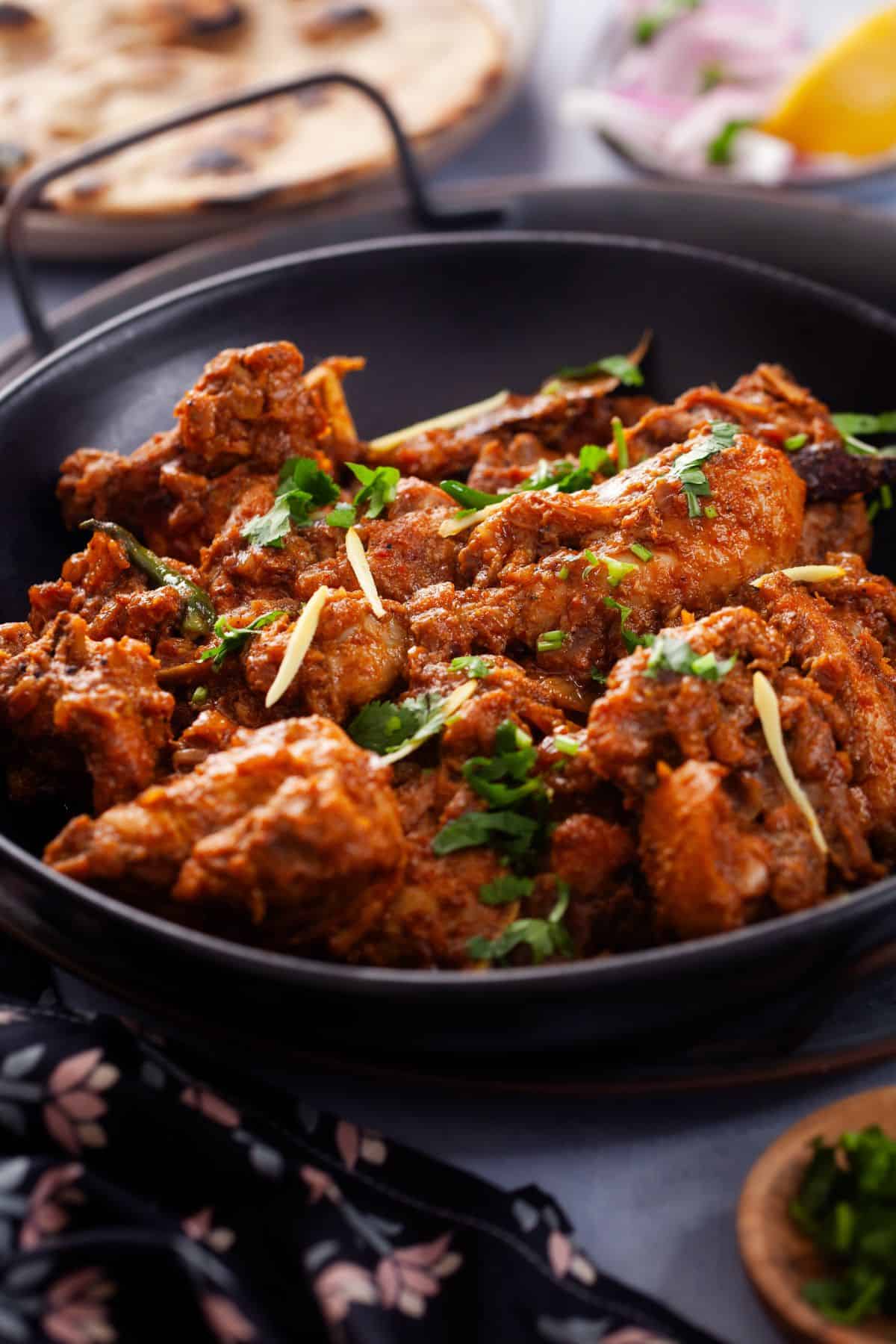 Side Image of chicken bhuna with tandoori roti in background. 