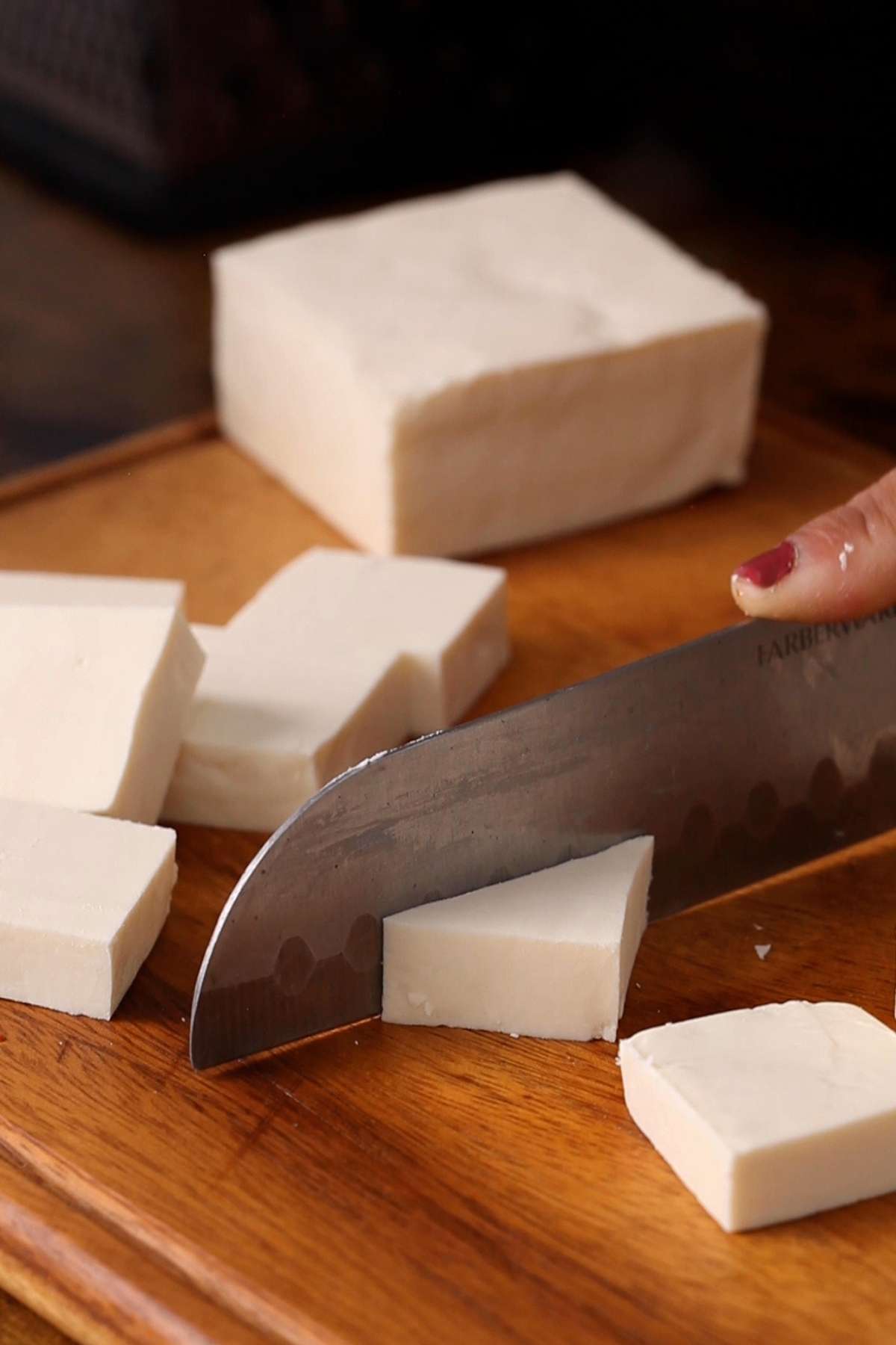 Cutting paneer with a sharp knife into triangular chunks.