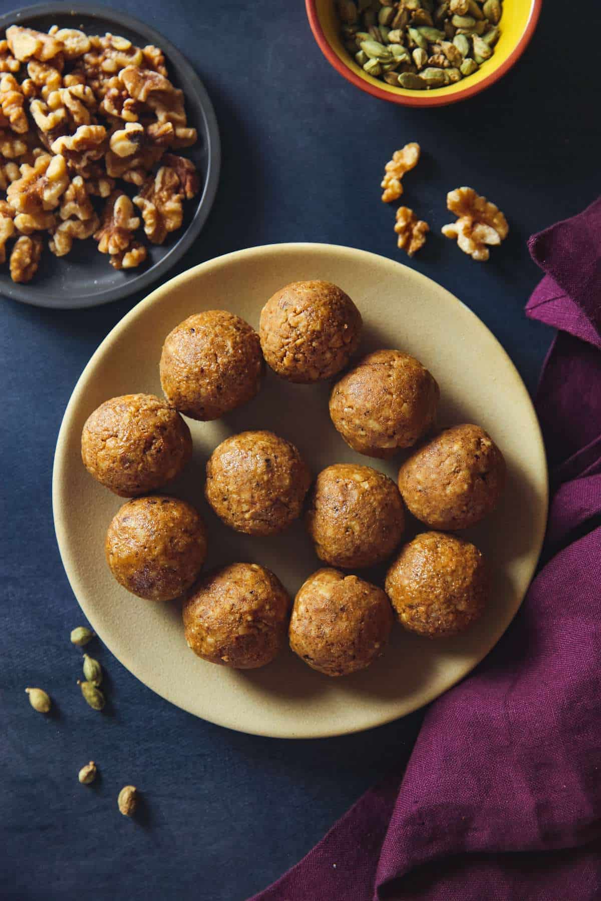 Walnut ladoos in a plate with cardamom and whole walnut pieces. 