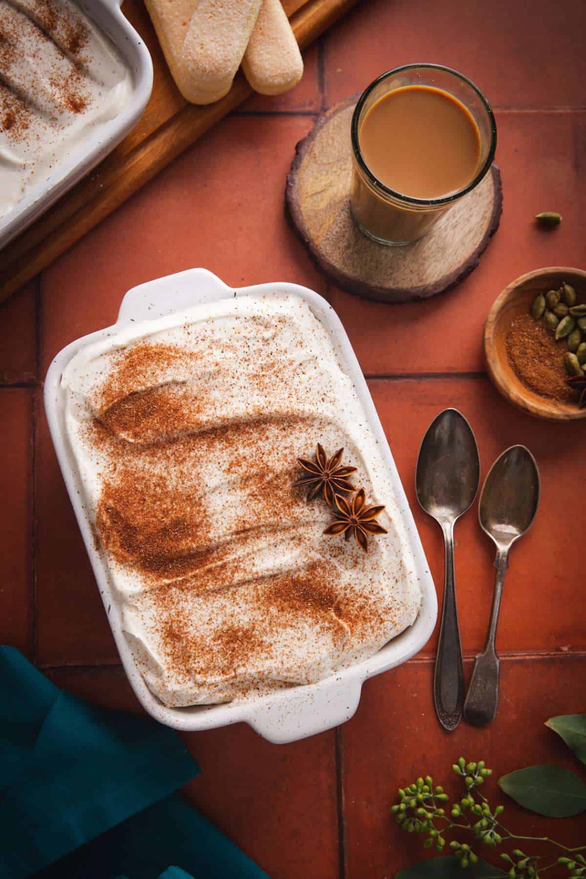 Masala Chai Tiramisu with cutting chai and spices on a terra-cotta background.