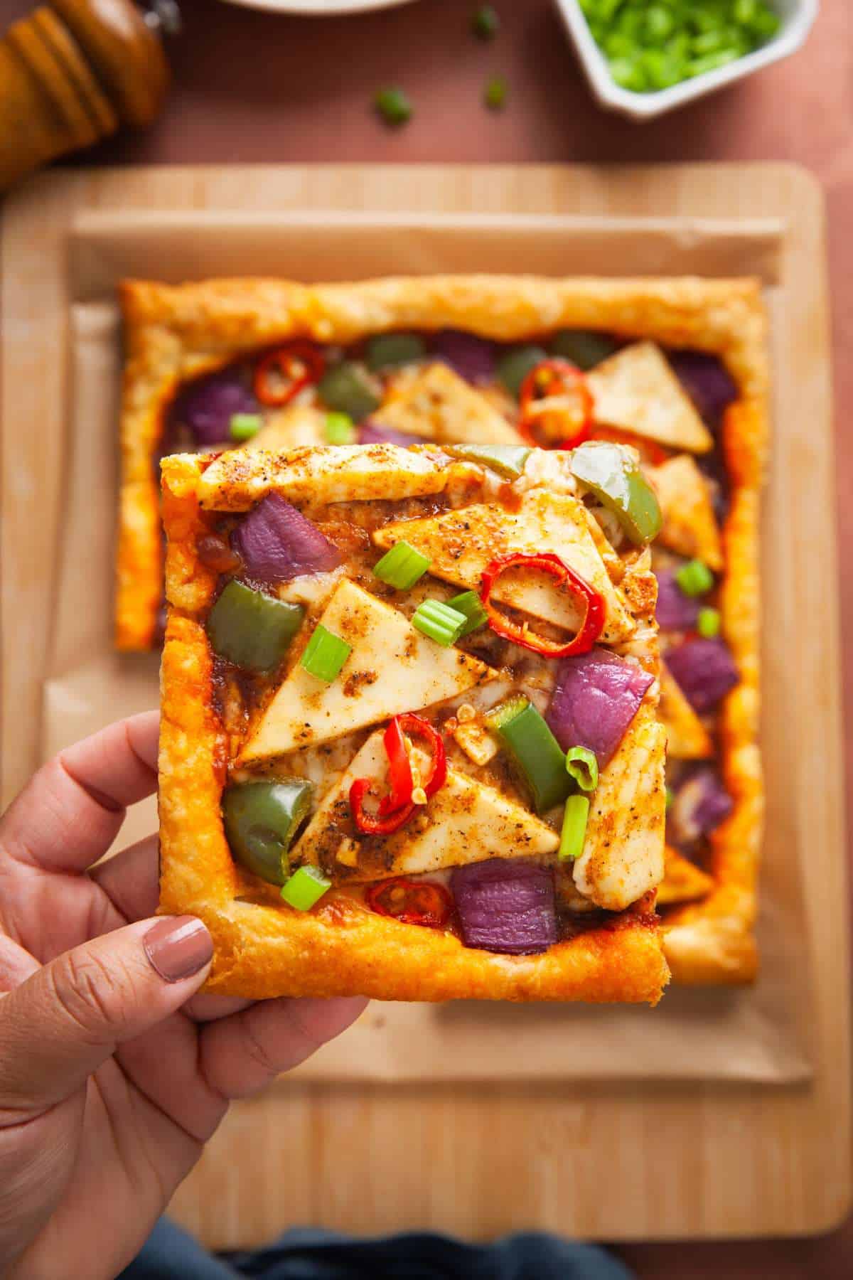 A slice of spicy smoky schezuapn paneer tart with veggies.